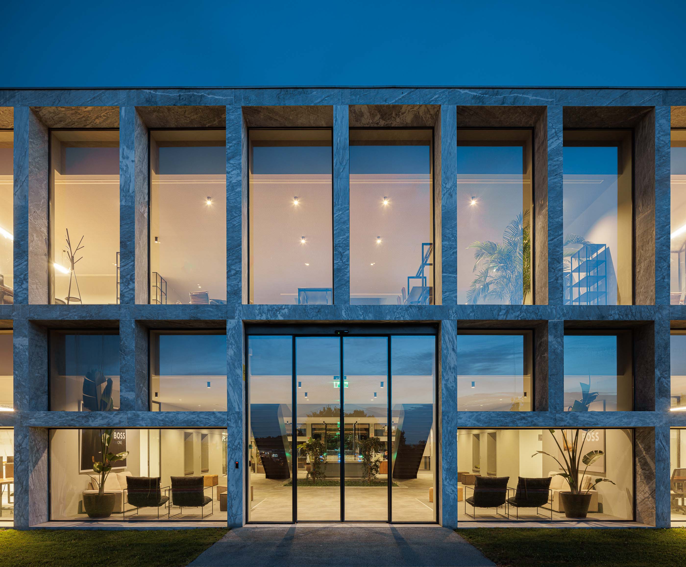 Edifício: Entrada do edifício com fachada em mármore e janelas amplas, iluminada à noite. — Metyis Digital Campus arquitetura UNUM - Oficina de Arquitetura em Gondomar