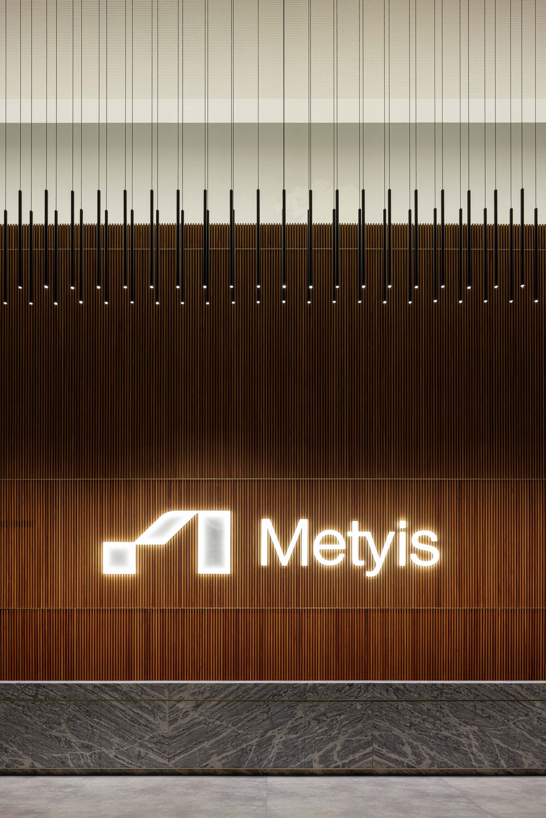 Hall de entrada: Detalhe da parede em madeira ripada com o logótipo da Metyis iluminado. — Metyis Digital Campus arquitetura UNUM - Oficina de Arquitetura em Gondomar