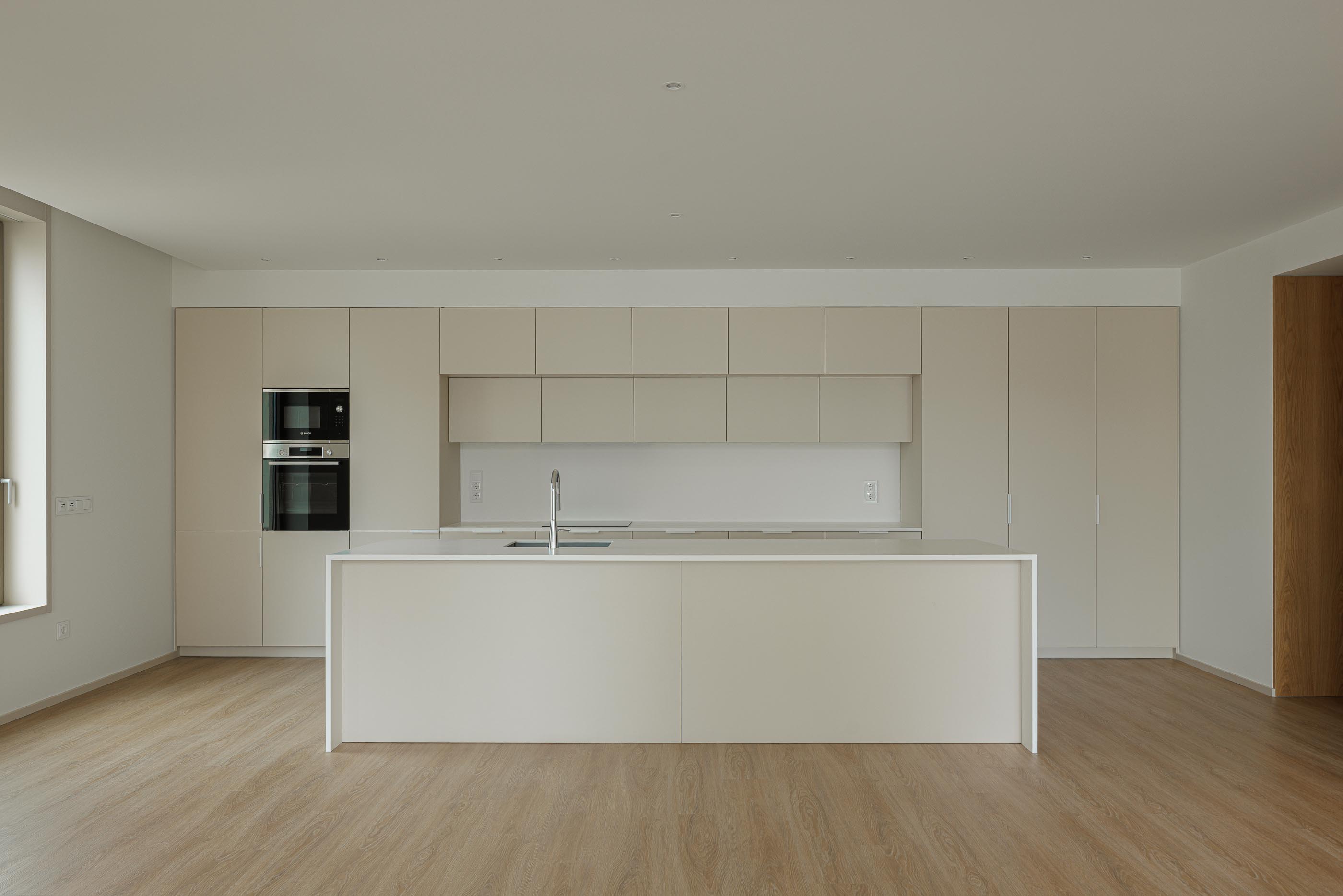 Cozinha: Cozinha com ilha central, armários bege e pavimento em madeira. — Macau Valley arquitetura hori-zonte em Vila Nova de Gaia