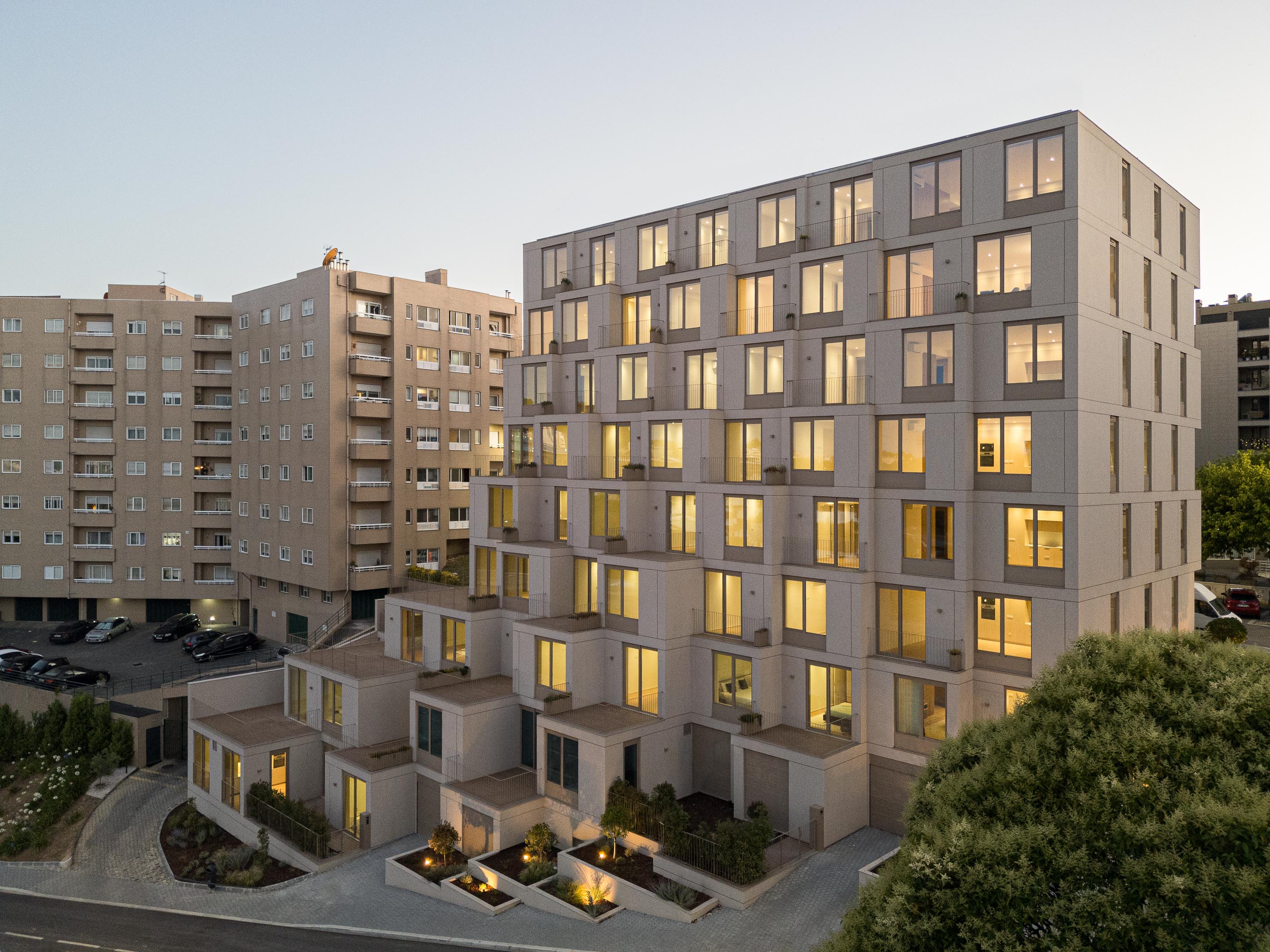 Fachada: Edifício de apartamentos com varandas escalonadas e iluminação interior ao entardecer. — Macau Valley arquitetura hori-zonte em Vila Nova de Gaia
