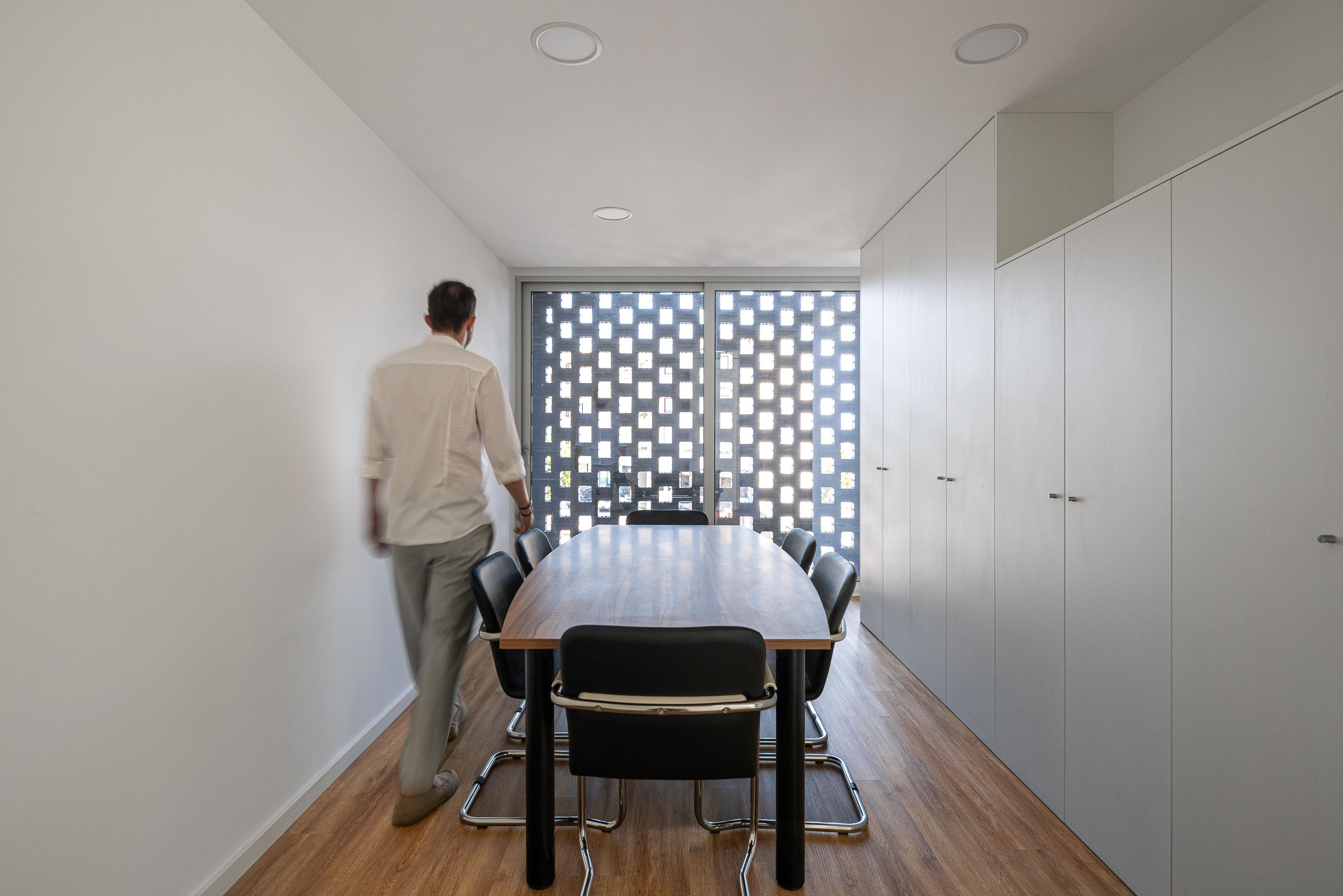 Sala de Reuniões: Mesa de madeira com cadeiras pretas, armários brancos embutidos e luz natural filtrada. — Junta de Freguesia de Vermoim arquitetura Rui Mendes Ribeiro Arquitecto em Vila Nova de Famalicão