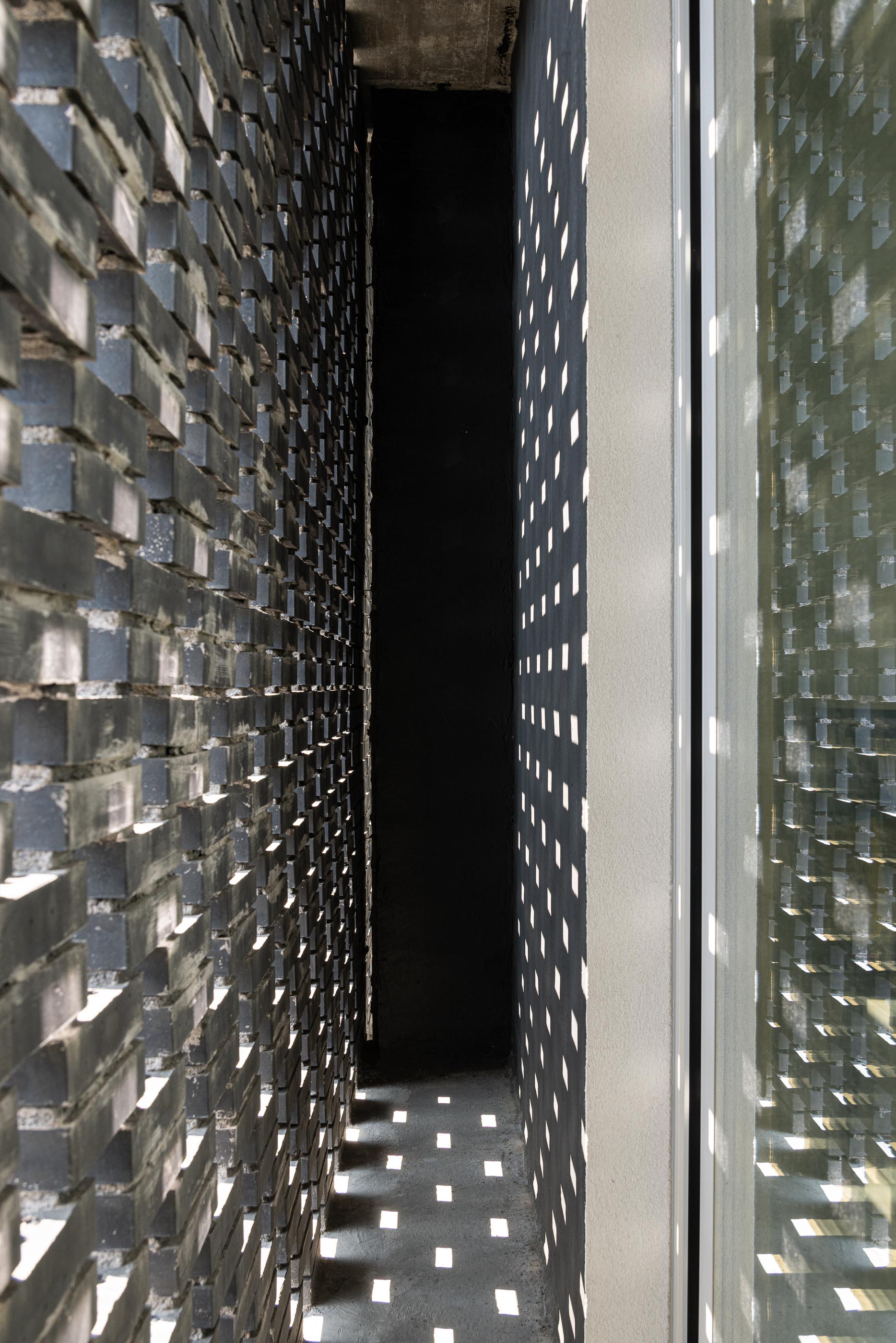 Exterior: Detalhe da parede de tijolo preto perfurado, com luz e sombra a criar padrões geométricos. — Junta de Freguesia de Vermoim arquitetura Rui Mendes Ribeiro Arquitecto em Vila Nova de Famalicão