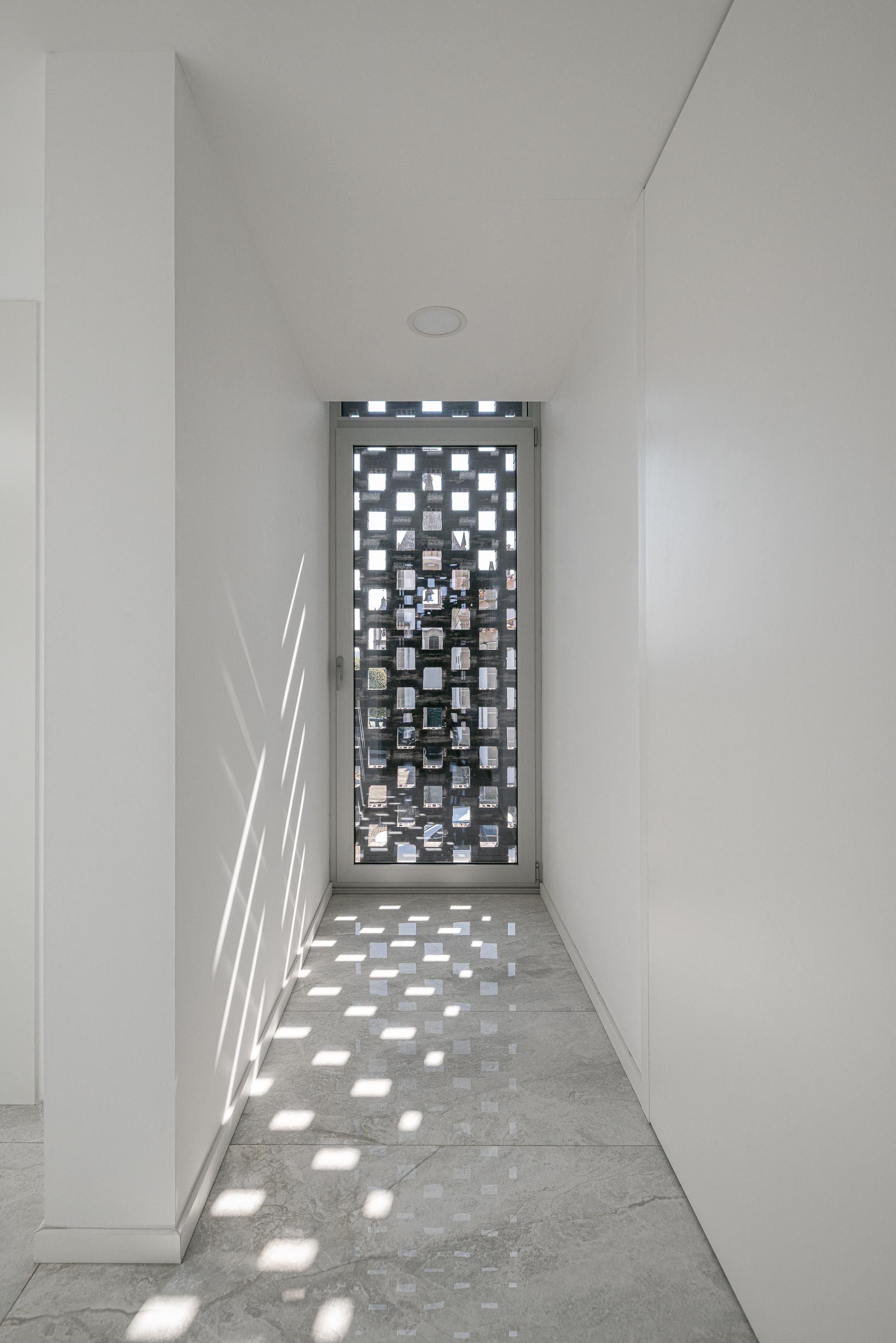 Corredor: Corredor branco com pavimento cinza e parede de tijolo perfurado ao fundo, criando jogo de luz e sombra. — Junta de Freguesia de Vermoim arquitetura Rui Mendes Ribeiro Arquitecto em Vila Nova de Famalicão
