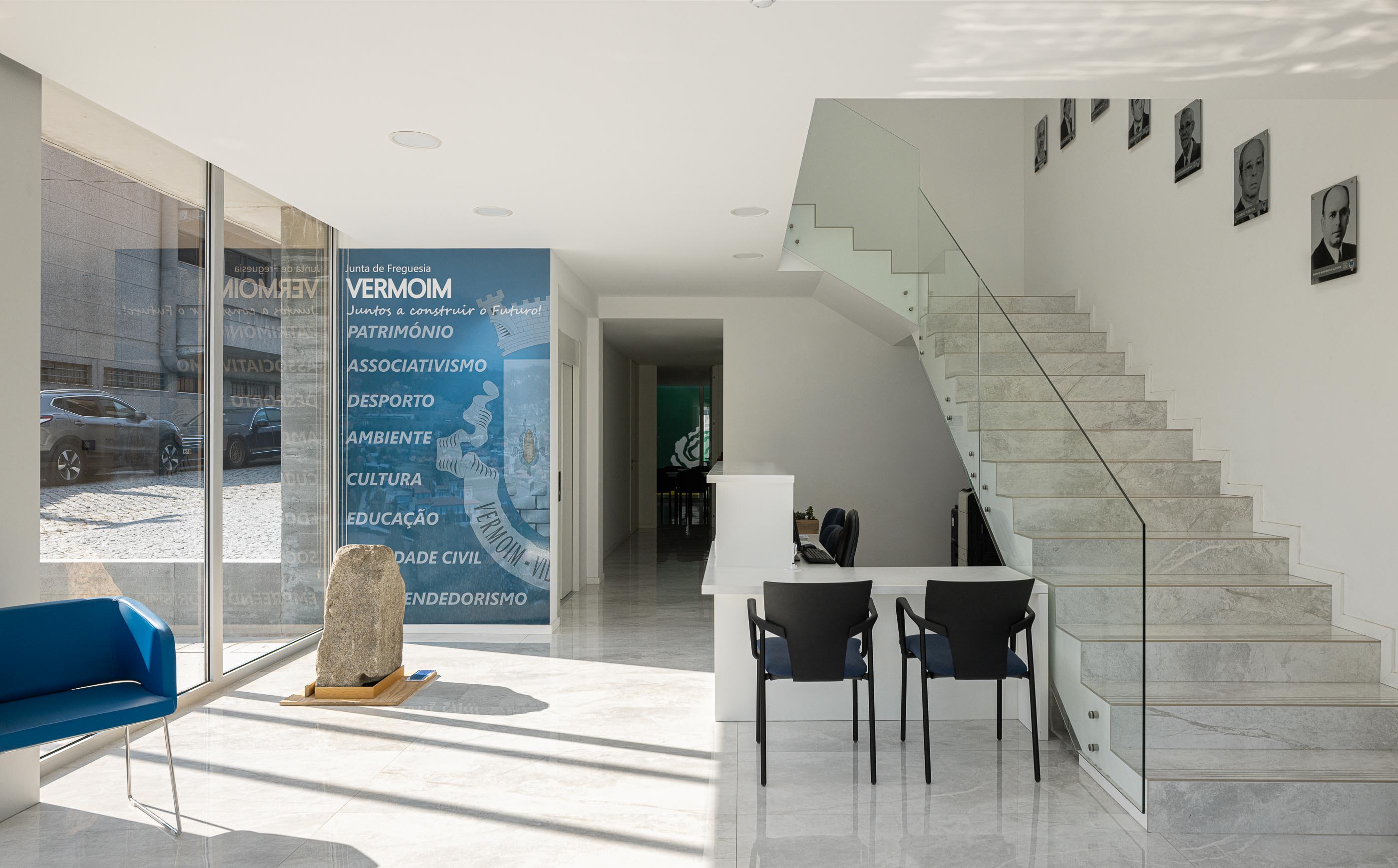 Hall: Hall de entrada com balcão de atendimento, escadas em mármore e zona de espera com cadeiras azuis. — Junta de Freguesia de Vermoim arquitetura Rui Mendes Ribeiro Arquitecto em Vila Nova de Famalicão