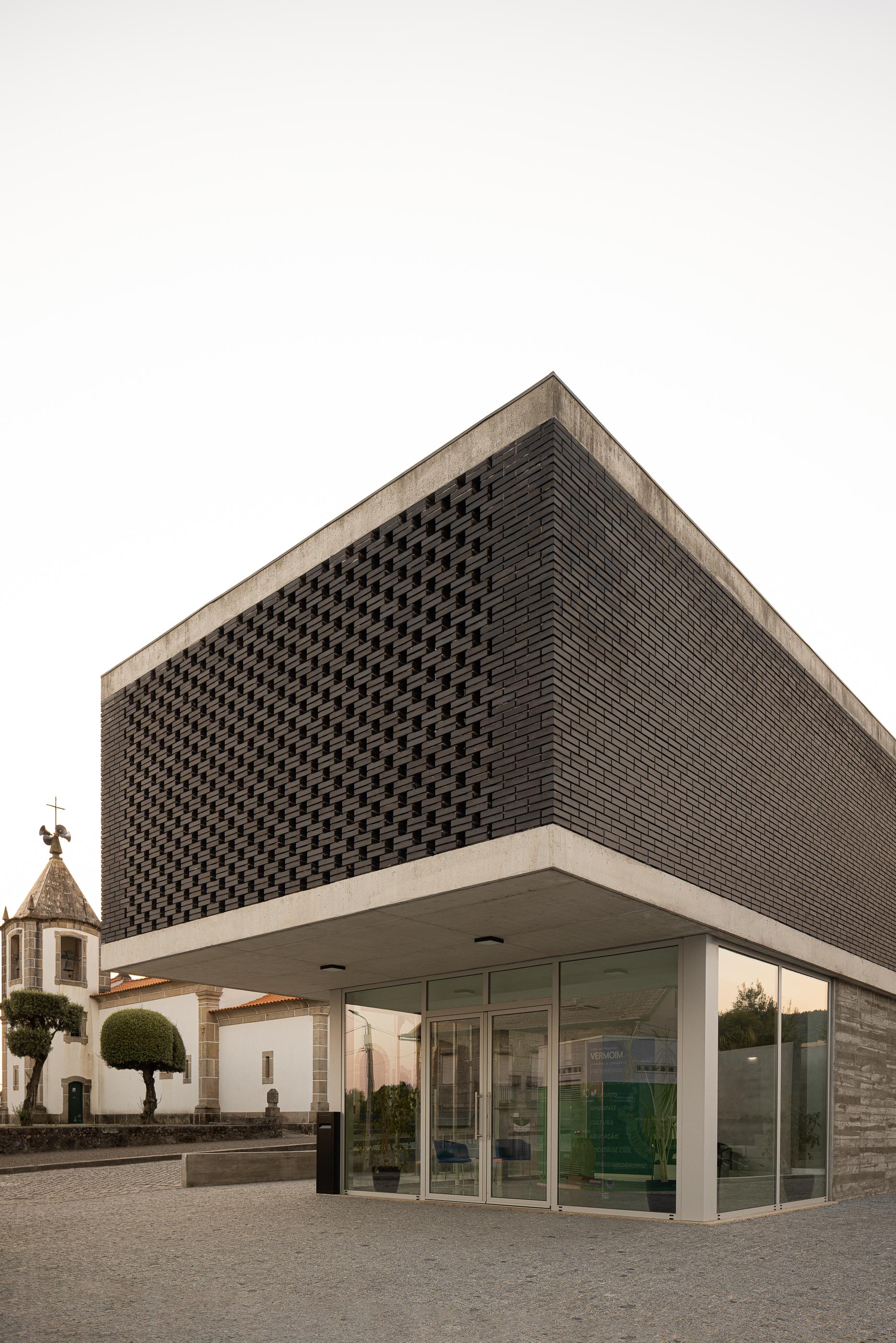 Exterior: Perspectiva do edifício da Junta de Freguesia com tijolo preto e fachada envidraçada. — Junta de Freguesia de Vermoim arquitetura Rui Mendes Ribeiro Arquitecto em Vila Nova de Famalicão