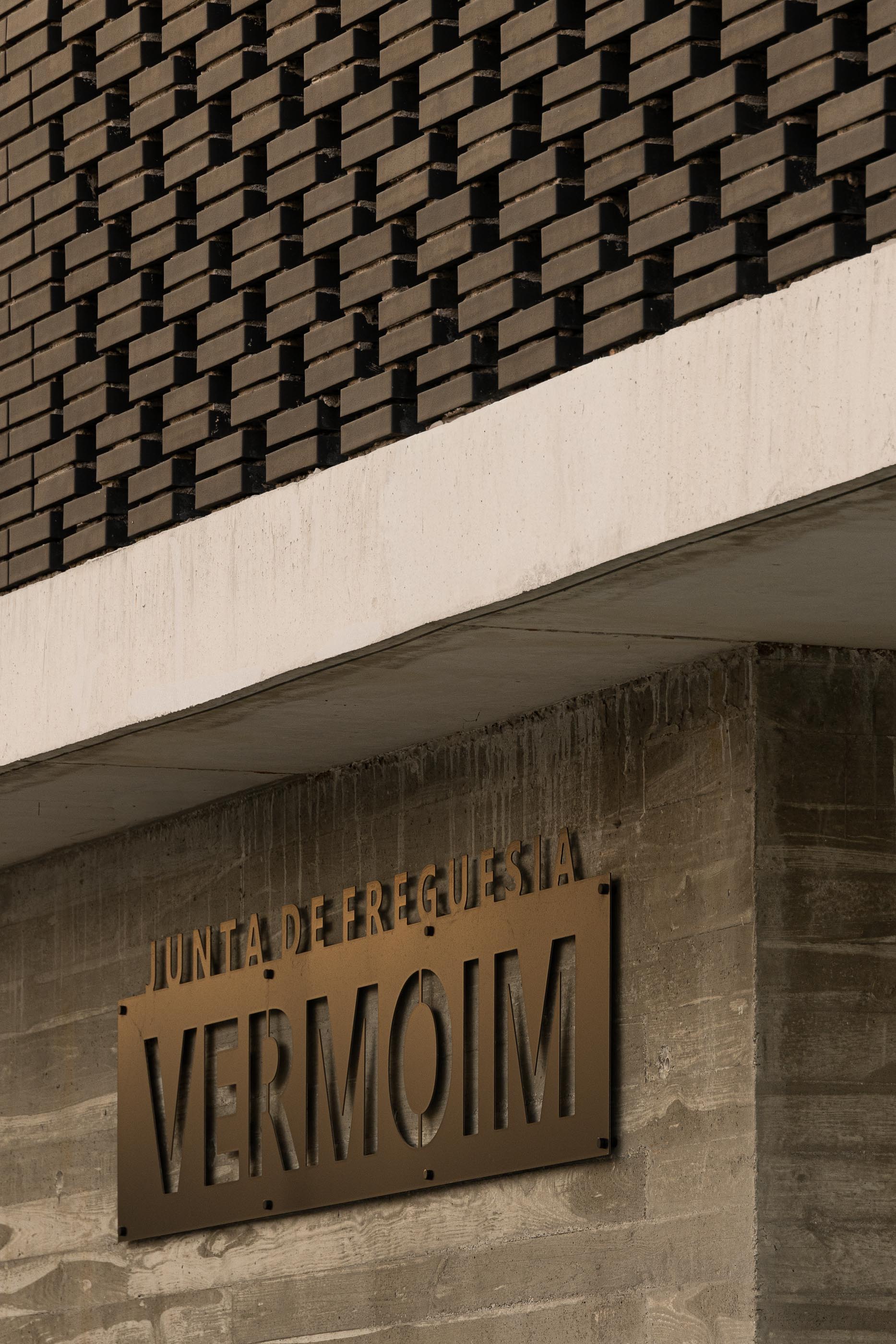 Fachada: Detalhe da placa "Junta de Freguesia de Vermoim" em betão aparente, com tijolo preto no topo. — Junta de Freguesia de Vermoim arquitetura Rui Mendes Ribeiro Arquitecto em Vila Nova de Famalicão