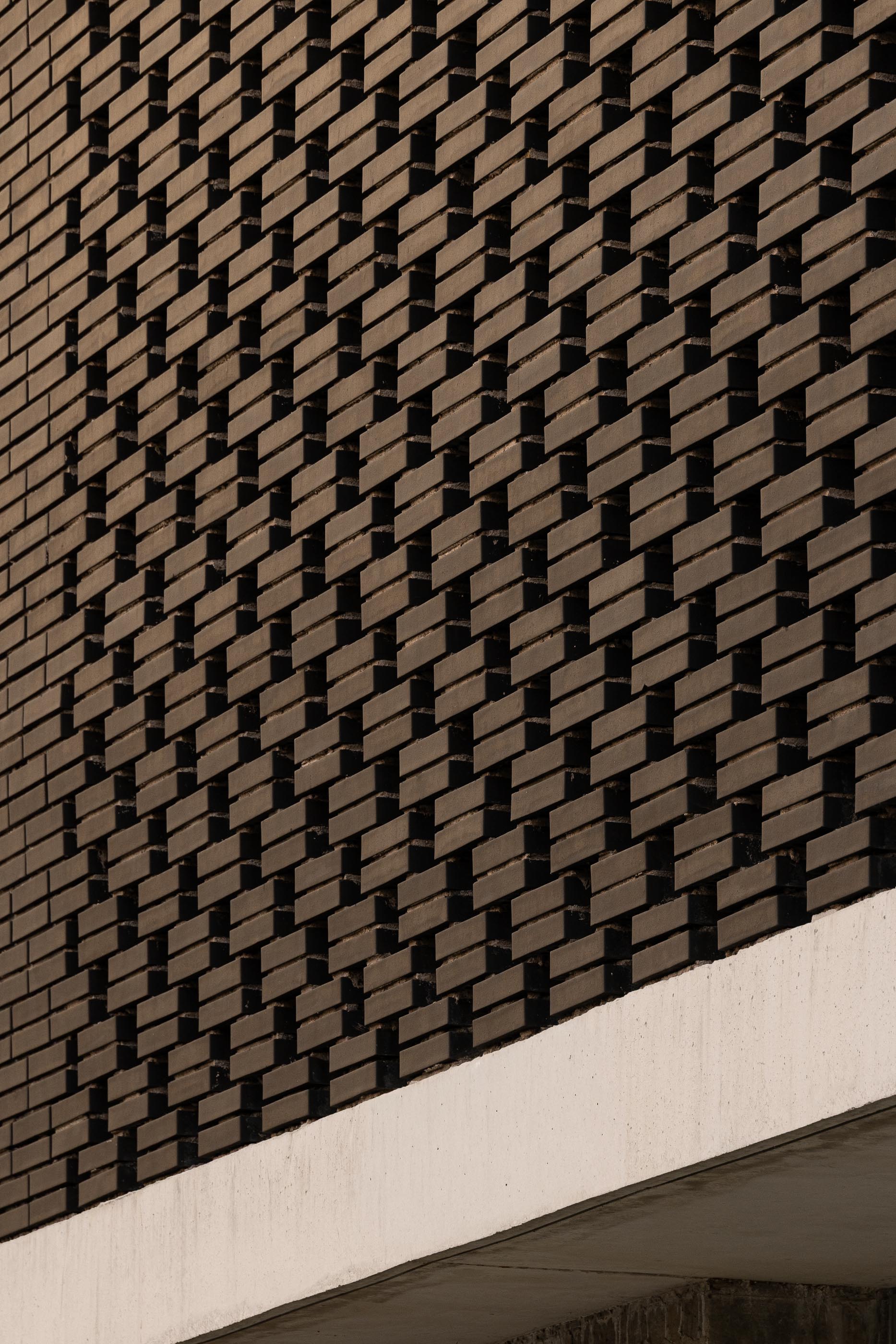 Fachada: Close-up da parede de tijolo preto perfurado, com junta de betão aparente. — Junta de Freguesia de Vermoim arquitetura Rui Mendes Ribeiro Arquitecto em Vila Nova de Famalicão