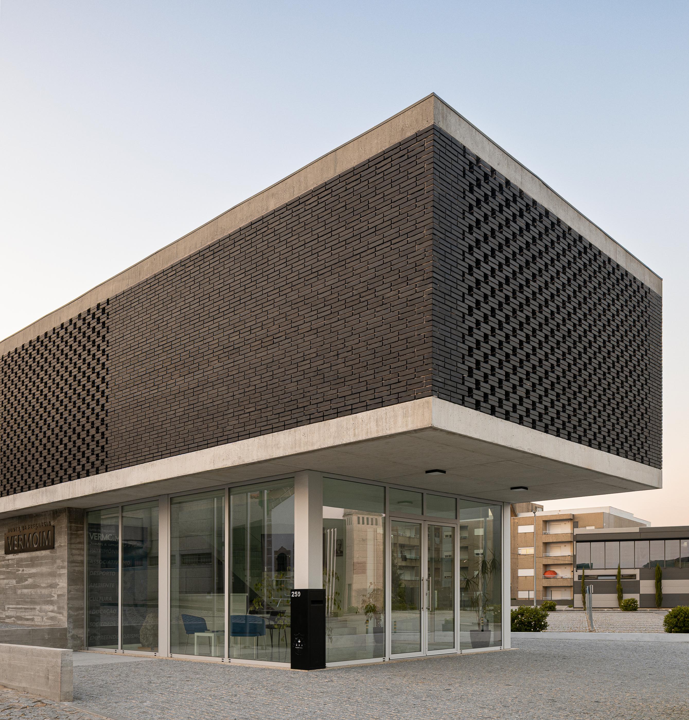 Fachada: Vista angular do edifício da Junta de Freguesia com tijolo preto e fachada envidraçada. — Junta de Freguesia de Vermoim arquitetura Rui Mendes Ribeiro Arquitecto em Vila Nova de Famalicão