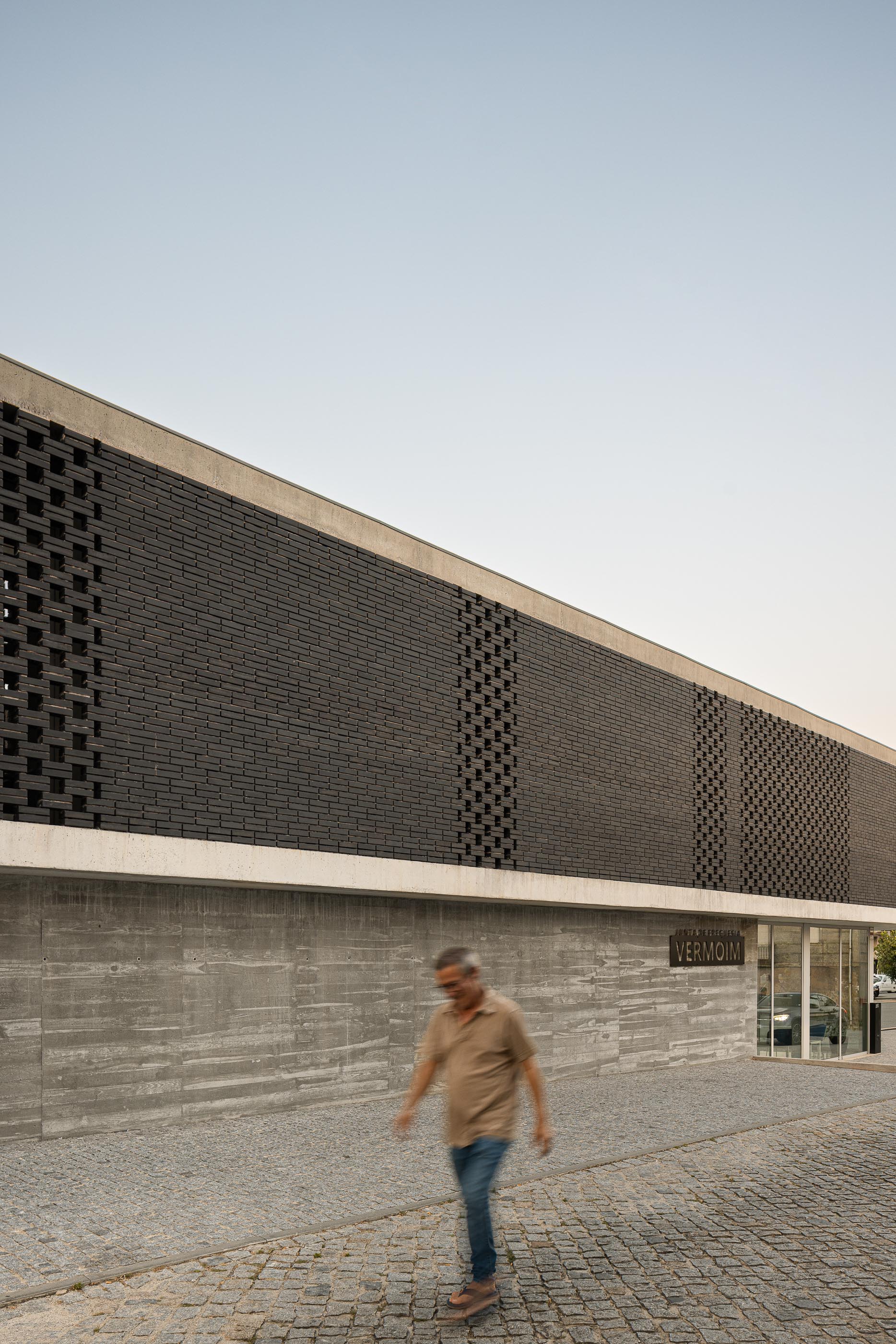 Fachada: Edifício da Junta de Freguesia com tijolo preto e base em betão, visto da rua. — Junta de Freguesia de Vermoim arquitetura Rui Mendes Ribeiro Arquitecto em Vila Nova de Famalicão