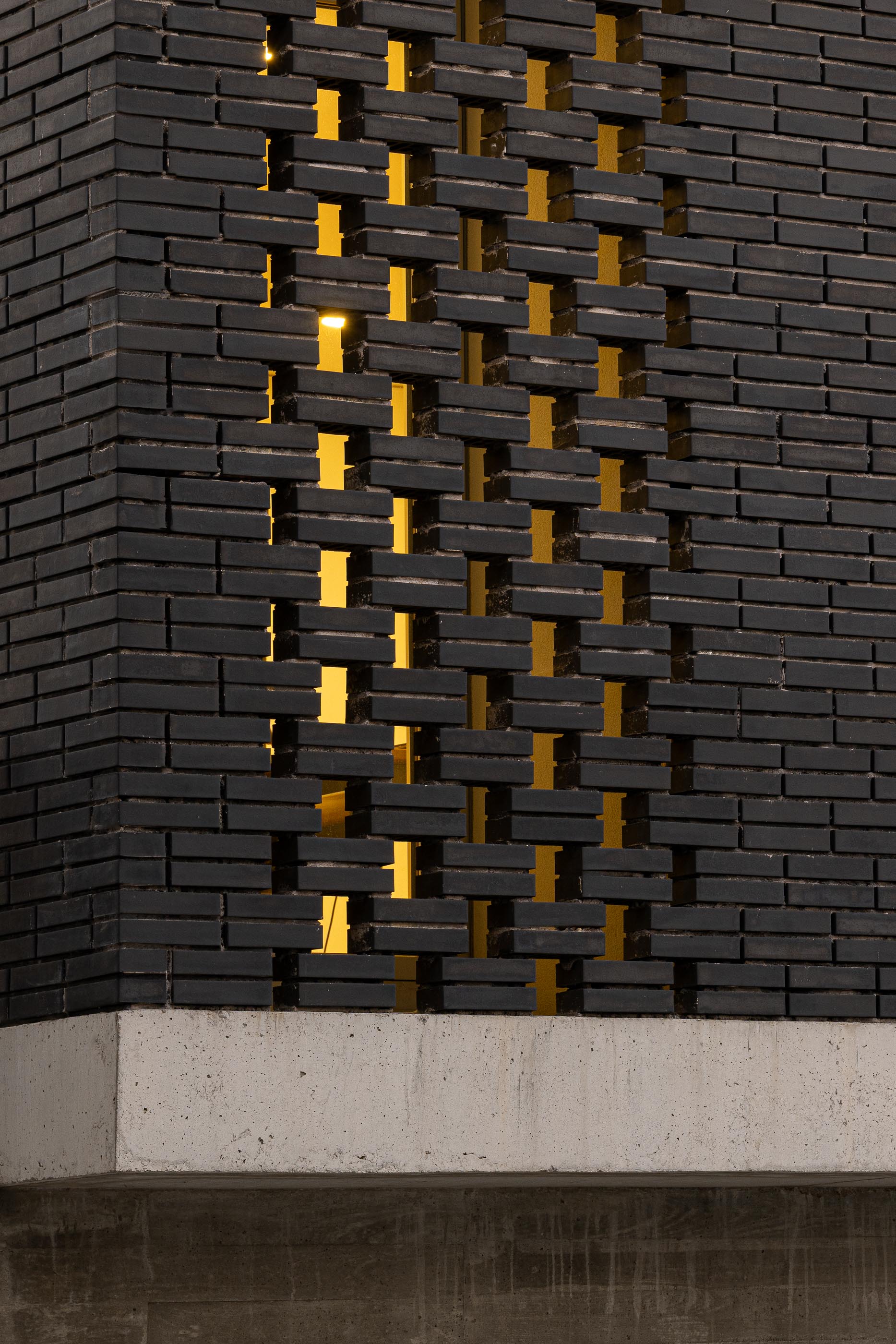 Fachada: Detalhe da parede de tijolo preto perfurado, com luz amarela a brilhar através dos orifícios. — Junta de Freguesia de Vermoim arquitetura Rui Mendes Ribeiro Arquitecto em Vila Nova de Famalicão