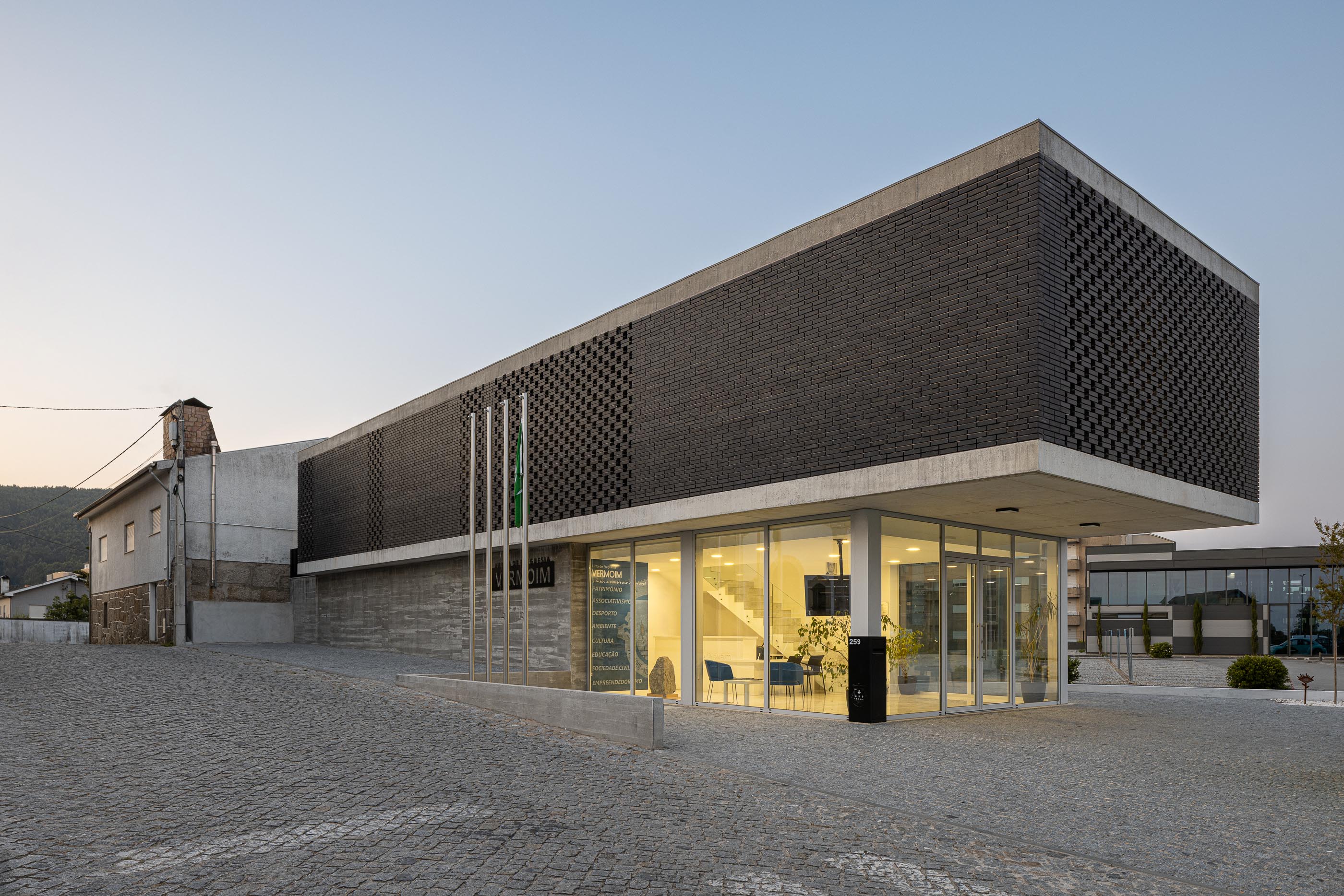 Fachada: Vista angular do edifício da Junta de Freguesia com tijolo preto e fachada envidraçada. — Junta de Freguesia de Vermoim arquitetura Rui Mendes Ribeiro Arquitecto em Vila Nova de Famalicão