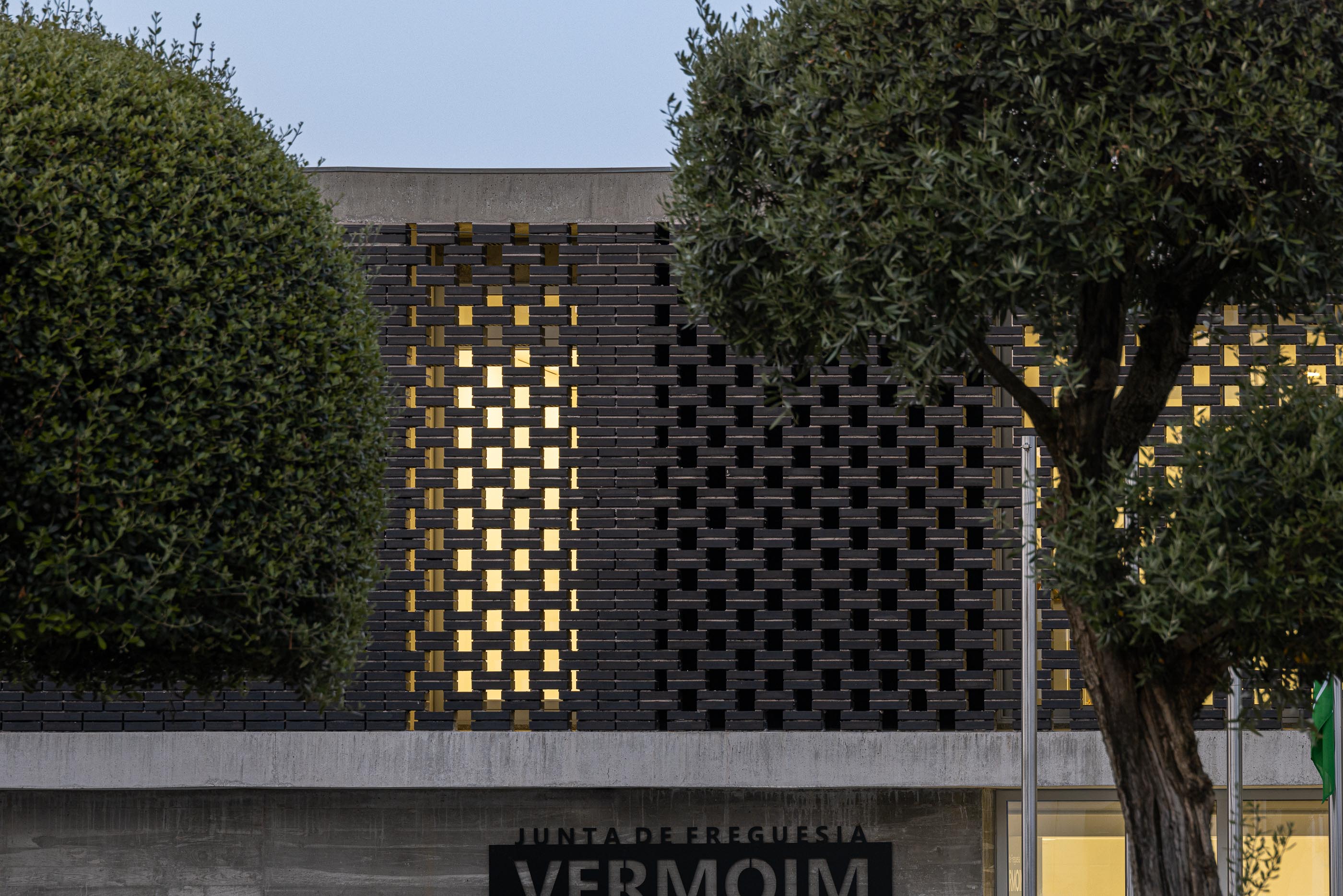 Fachada: Detalhe da parede de tijolo preto perfurado, com iluminação interior visível. — Junta de Freguesia de Vermoim arquitetura Rui Mendes Ribeiro Arquitecto em Vila Nova de Famalicão