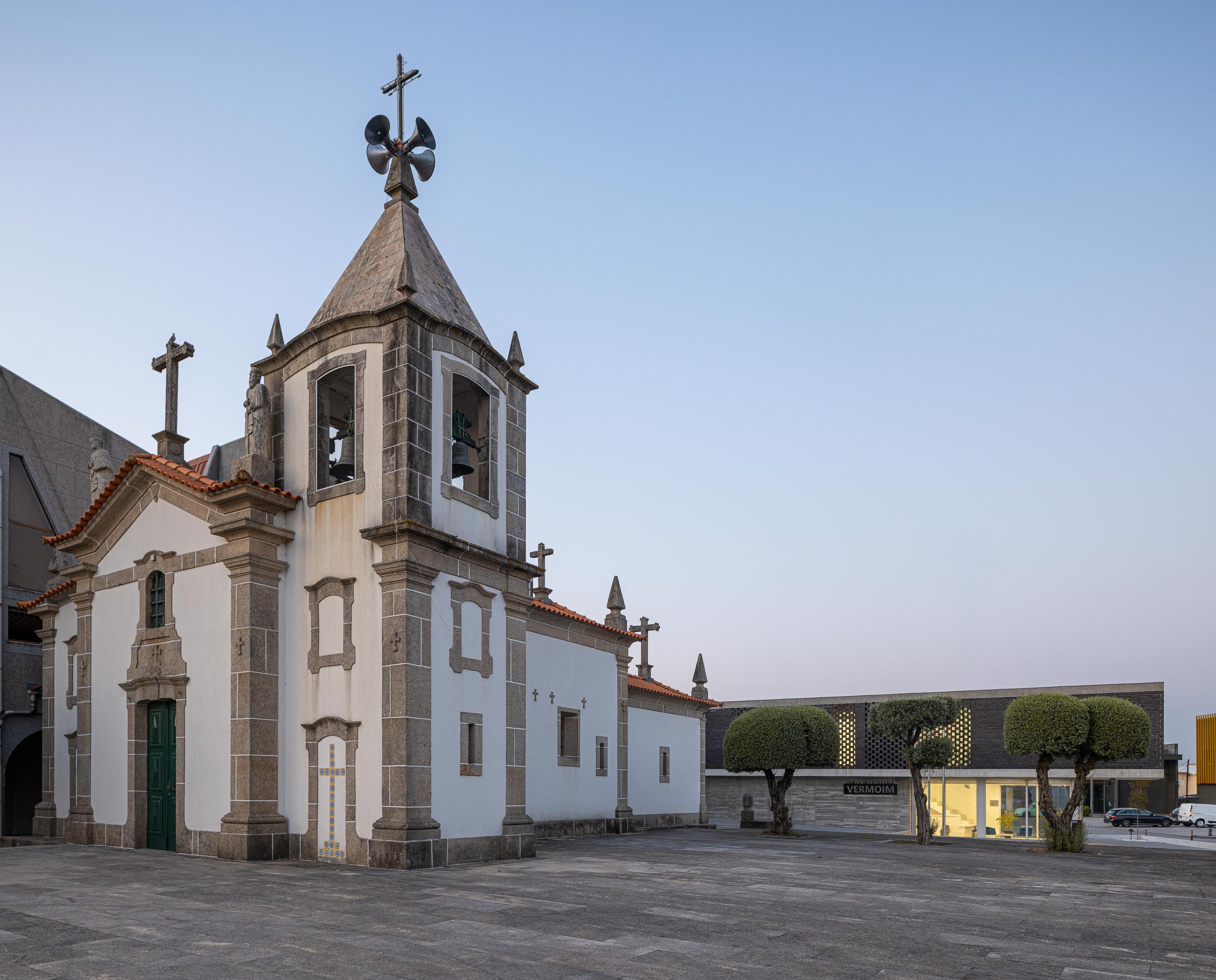Exterior: Igreja matriz e edifício da Junta de Freguesia vistos da praça, ao entardecer. — Junta de Freguesia de Vermoim arquitetura Rui Mendes Ribeiro Arquitecto em Vila Nova de Famalicão