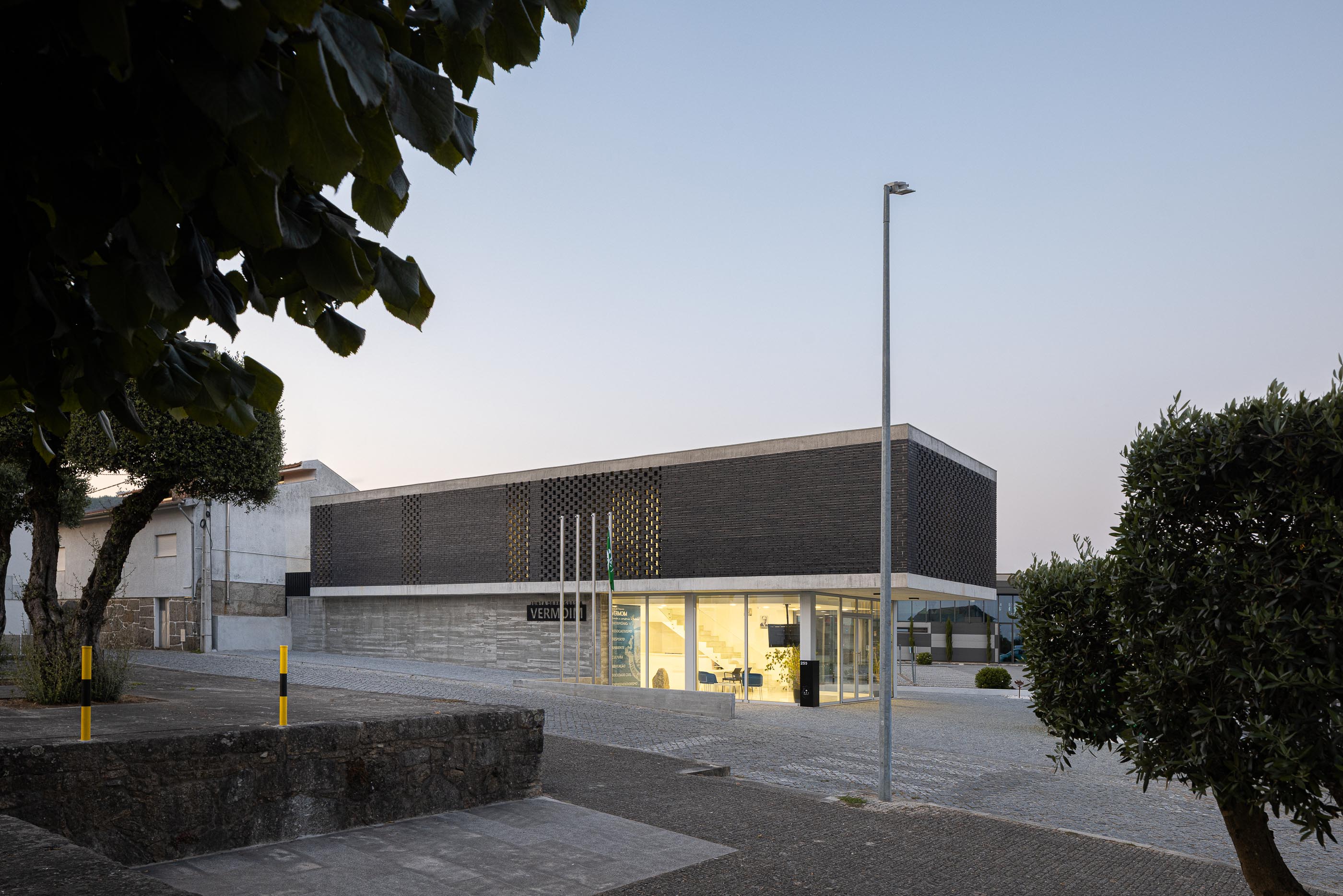 Fachada: Edifício da Junta de Freguesia com tijolo preto e fachada envidraçada, visto da rua. — Junta de Freguesia de Vermoim arquitetura Rui Mendes Ribeiro Arquitecto em Vila Nova de Famalicão