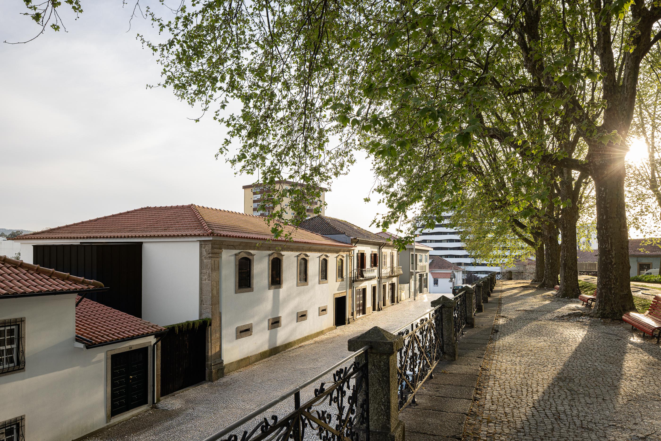 Paisagem: Vista da moradia com telhado de telha, fachada branca e anexo moderno preto, enquadrada por árvores e passeio em calçada. — Moradia do Retiro arquitetura Ricardo Azevedo Arquitecto em Santo Tirso
