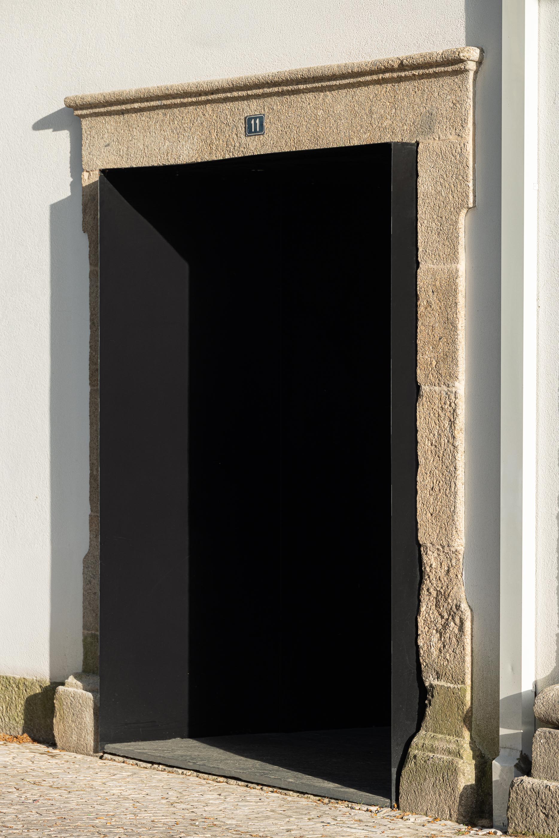 Entrada secundária: Porta preta minimalista emoldurada por cantaria tradicional, número 11 visível. — Moradia do Retiro arquitetura Ricardo Azevedo Arquitecto em Santo Tirso
