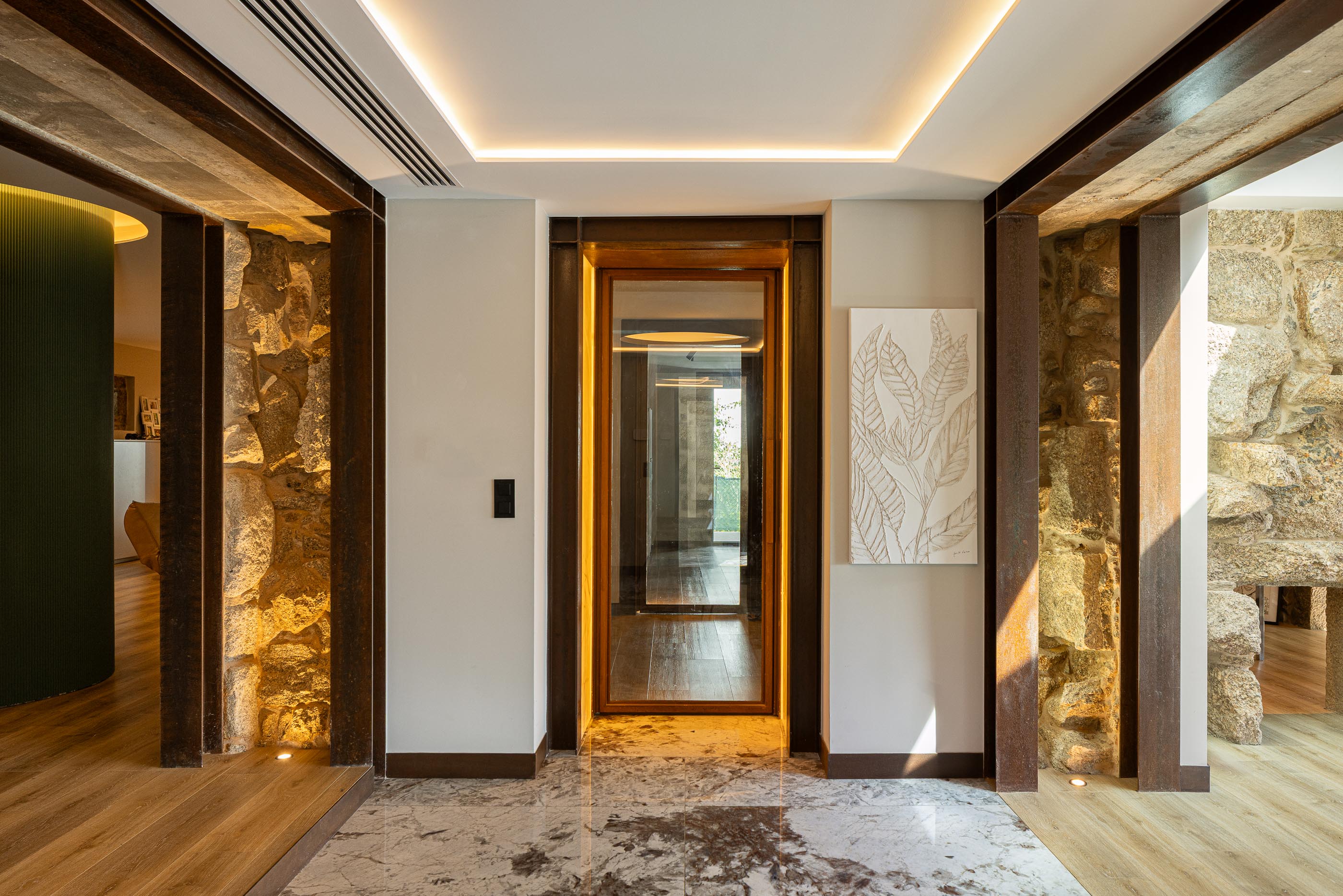 Hall de entrada: Pavimento em mármore, paredes em pedra e madeira, iluminação embutida e obra de arte minimalista. — Moradia do Retiro arquitetura Ricardo Azevedo Arquitecto em Santo Tirso