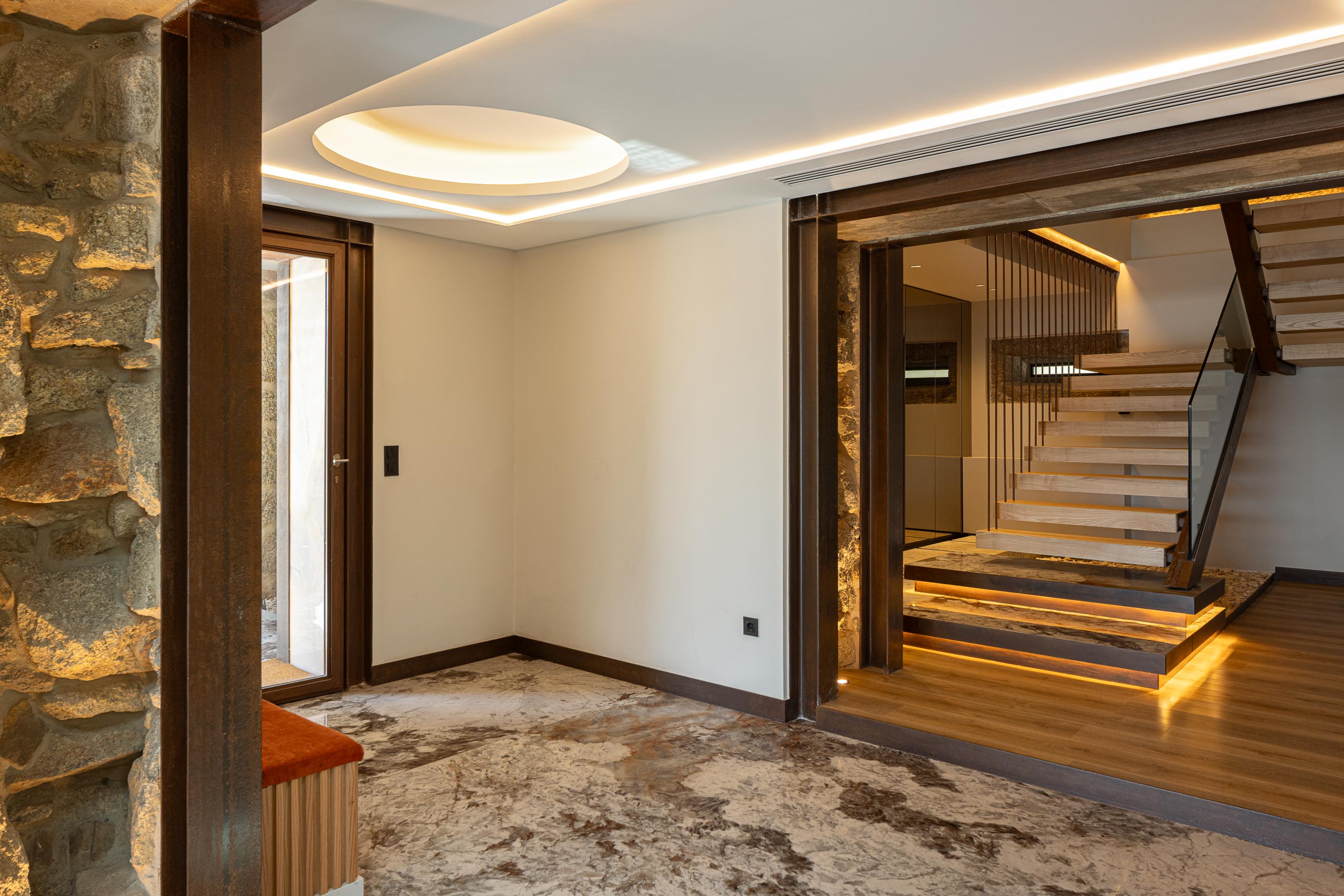 Hall de entrada: Pavimento em mármore, paredes em pedra e escadas de madeira com guarda em vidro. — Moradia do Retiro arquitetura Ricardo Azevedo Arquitecto em Santo Tirso