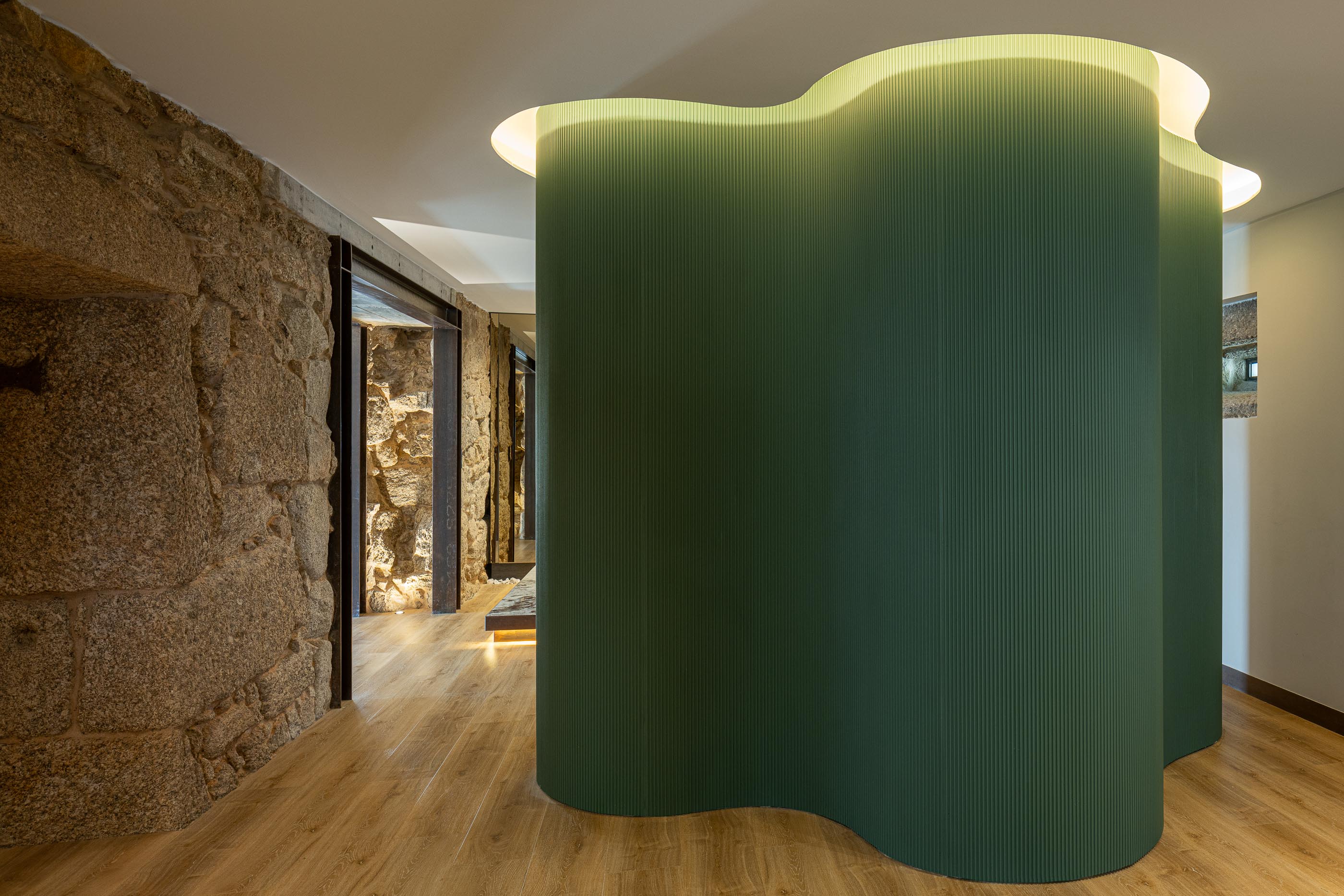 Corredor: Parede ondulada verde, pavimento em madeira e parede em pedra rústica. — Moradia do Retiro arquitetura Ricardo Azevedo Arquitecto em Santo Tirso