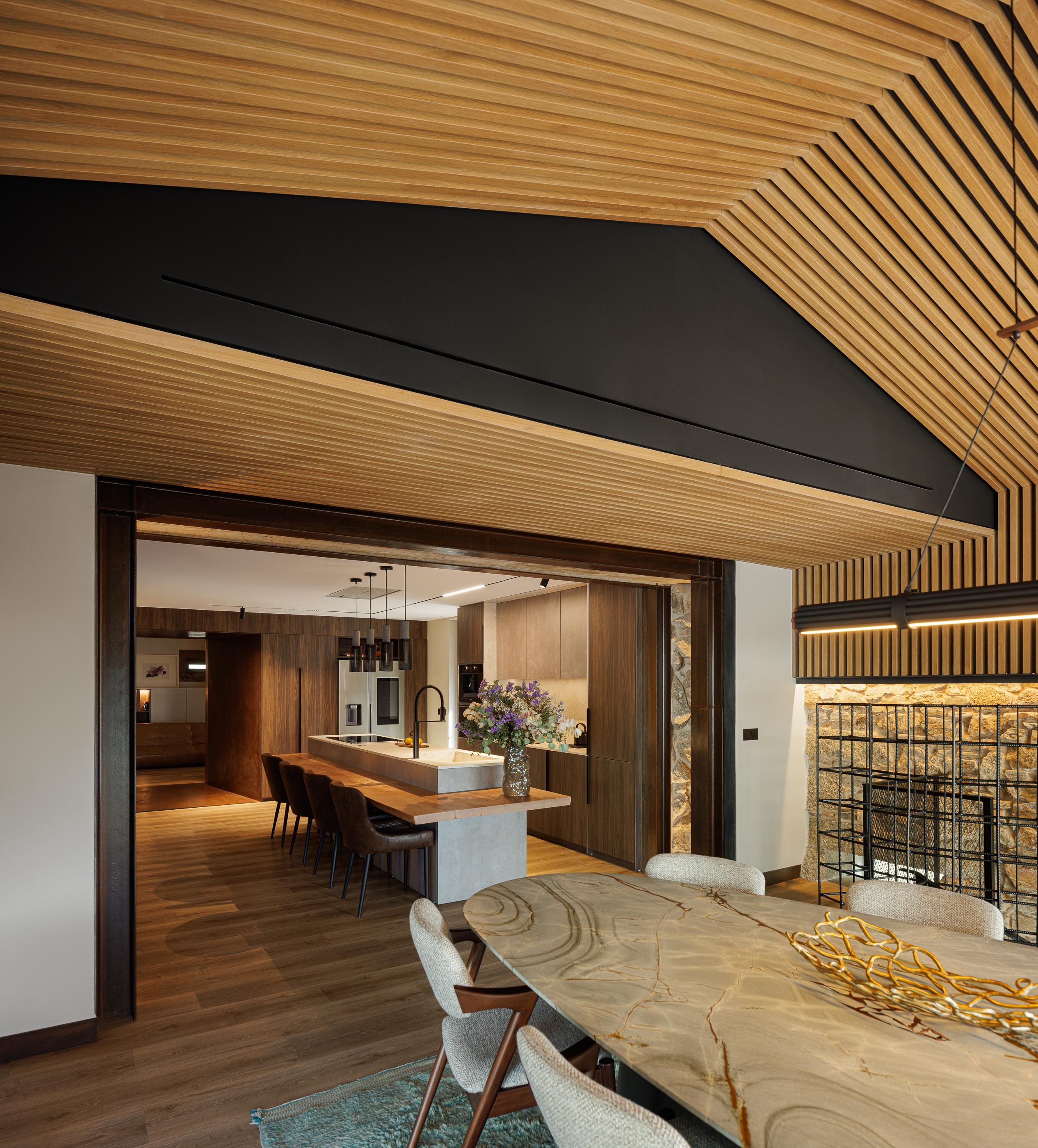 Sala de jantar/cozinha: Teto em madeira, mesa de jantar em pedra, cadeiras estofadas e iluminação suspensa. — Moradia do Retiro arquitetura Ricardo Azevedo Arquitecto em Santo Tirso