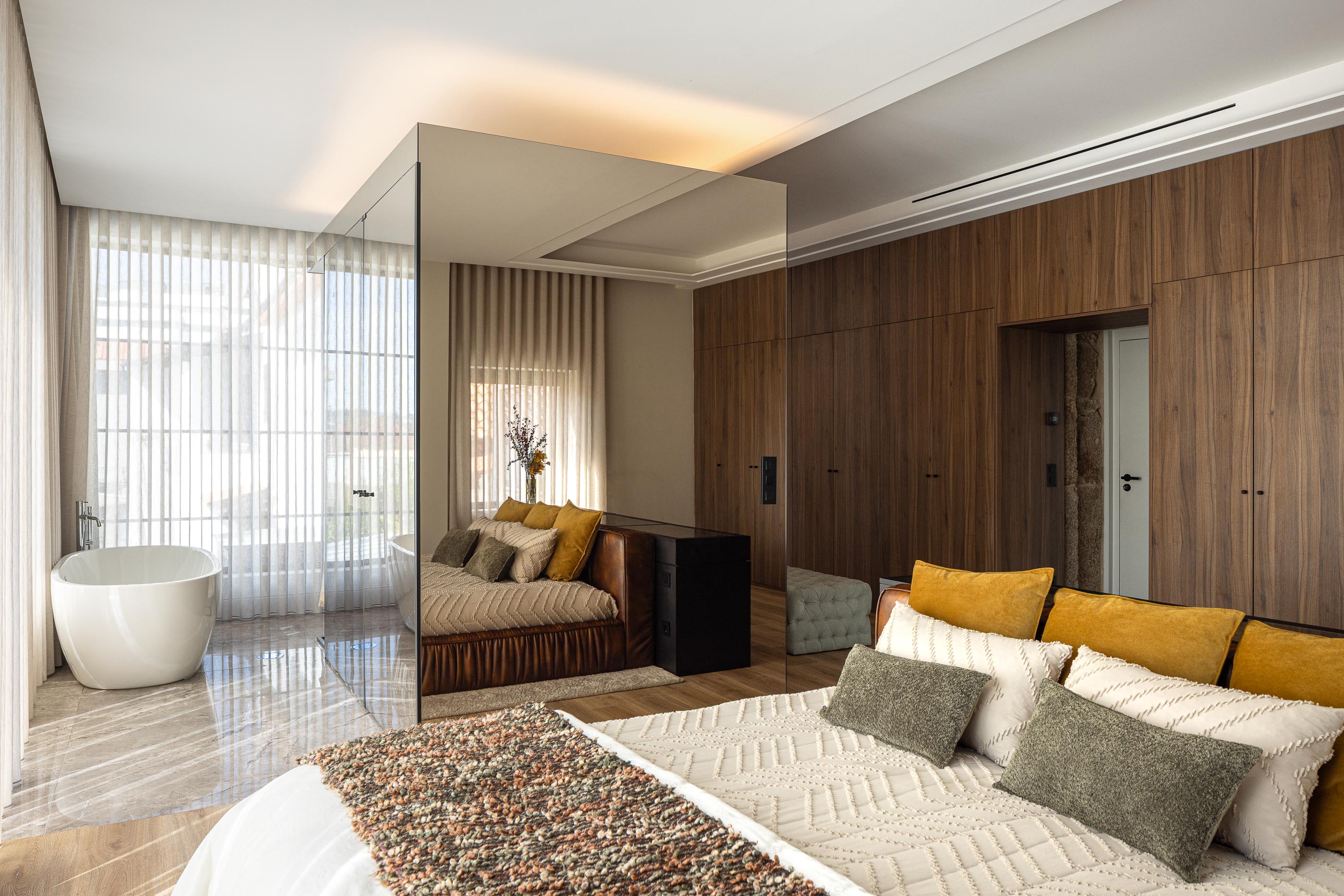 Suite: Cama de casal, banheira independente, roupeiro embutido e cortinas claras. — Moradia do Retiro arquitetura Ricardo Azevedo Arquitecto em Santo Tirso