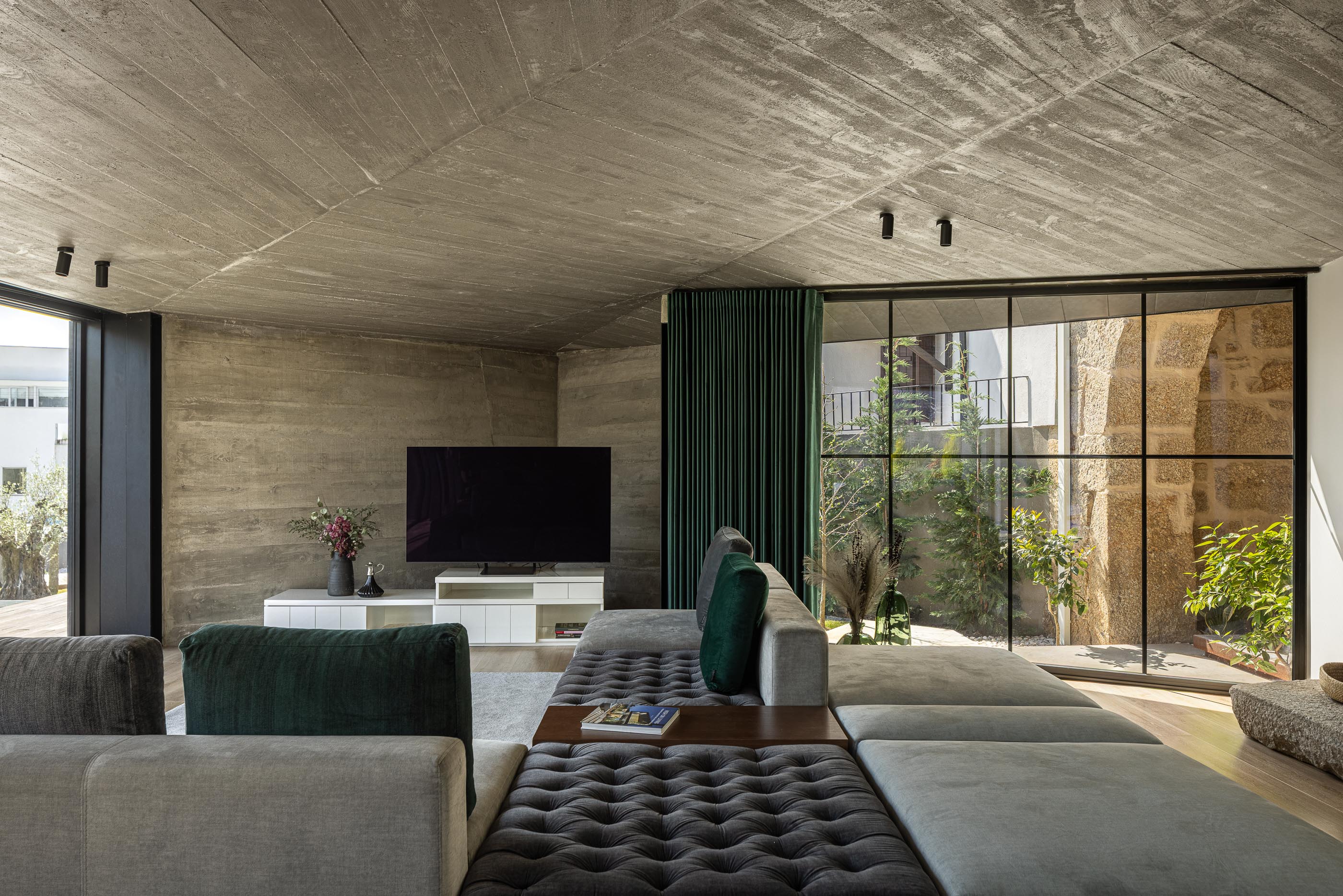 Sala de estar: Sofá modular cinza, teto em betão aparente, lareira moderna e grandes janelas. — Moradia do Retiro arquitetura Ricardo Azevedo Arquitecto em Santo Tirso