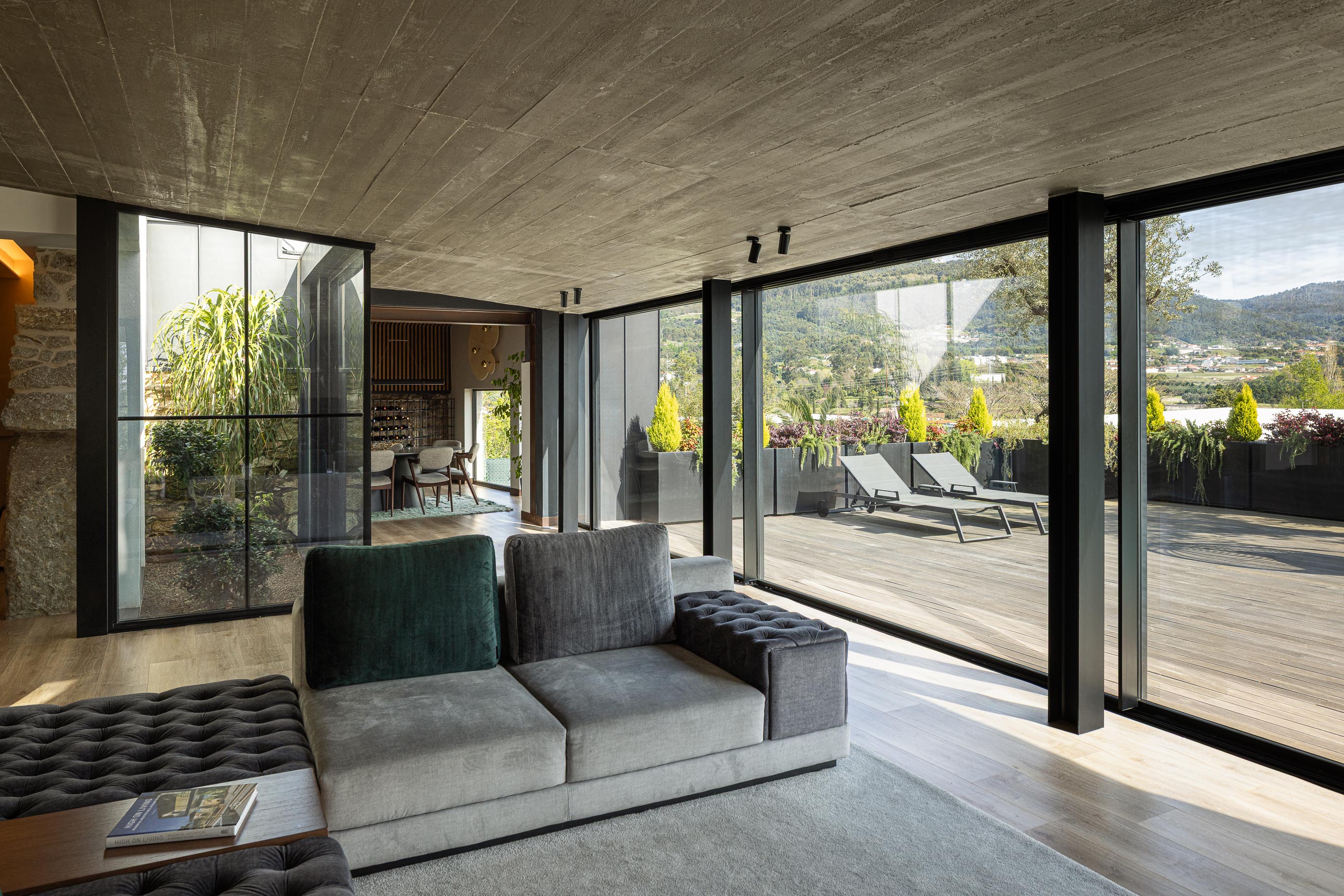 Sala de estar: Sofá cinza, pavimento em madeira, grandes janelas com vista para o terraço e jardim. — Moradia do Retiro arquitetura Ricardo Azevedo Arquitecto em Santo Tirso