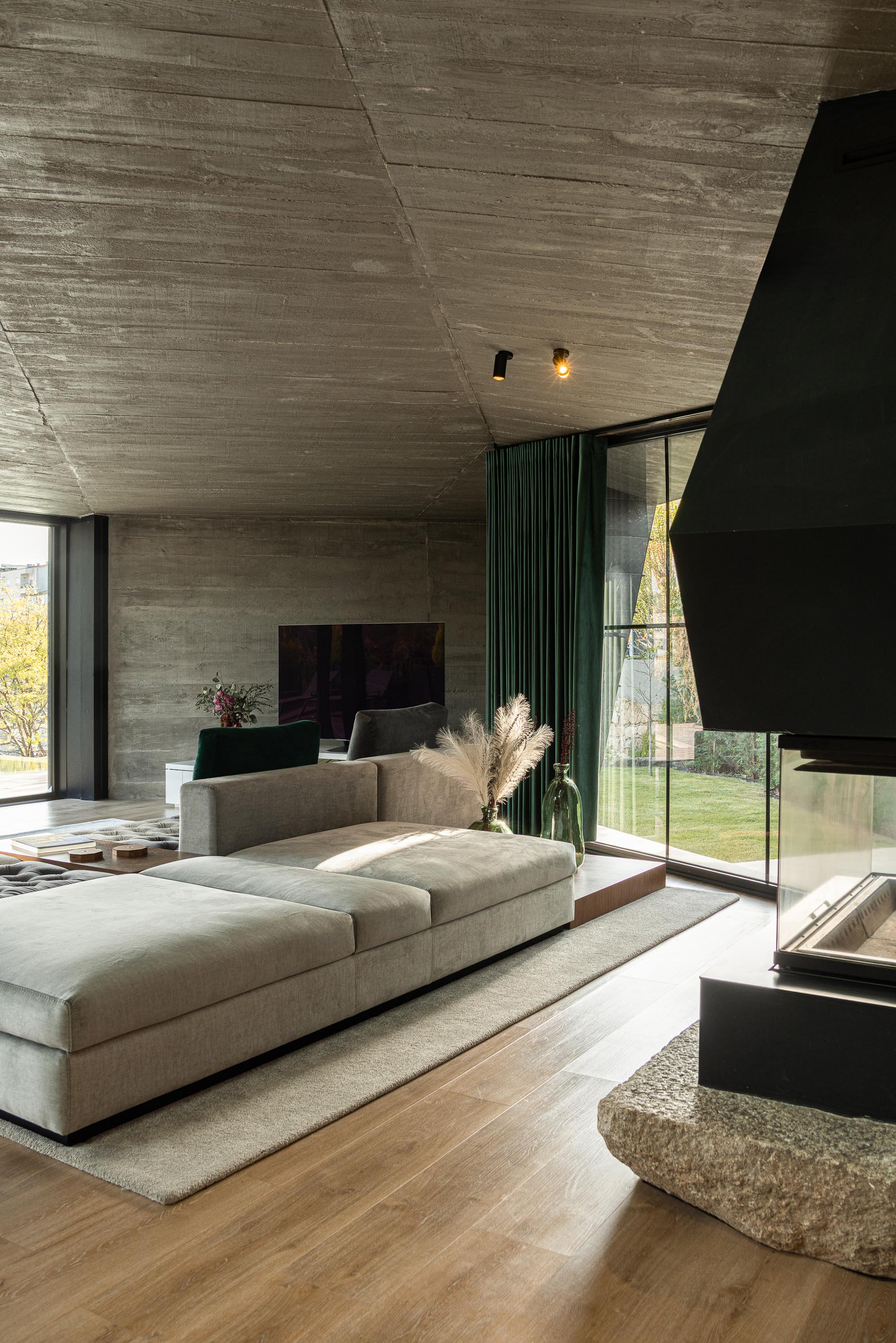 Sala de estar: Lareira preta, sofá cinza, teto em betão aparente e vista para o jardim. — Moradia do Retiro arquitetura Ricardo Azevedo Arquitecto em Santo Tirso