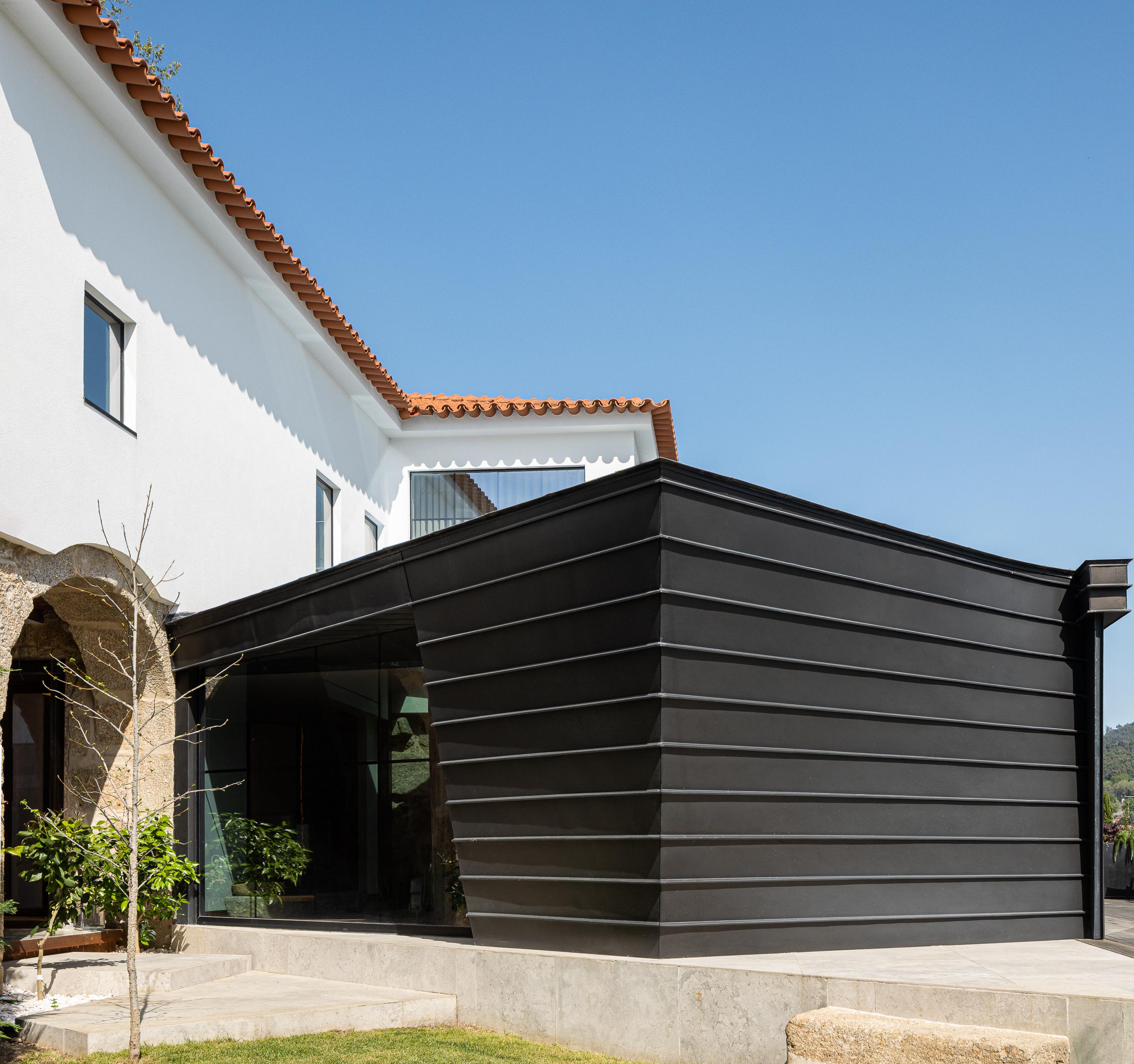 Exterior: Anexo moderno com revestimento metálico preto, janelas amplas e jardim. — Moradia do Retiro arquitetura Ricardo Azevedo Arquitecto em Santo Tirso