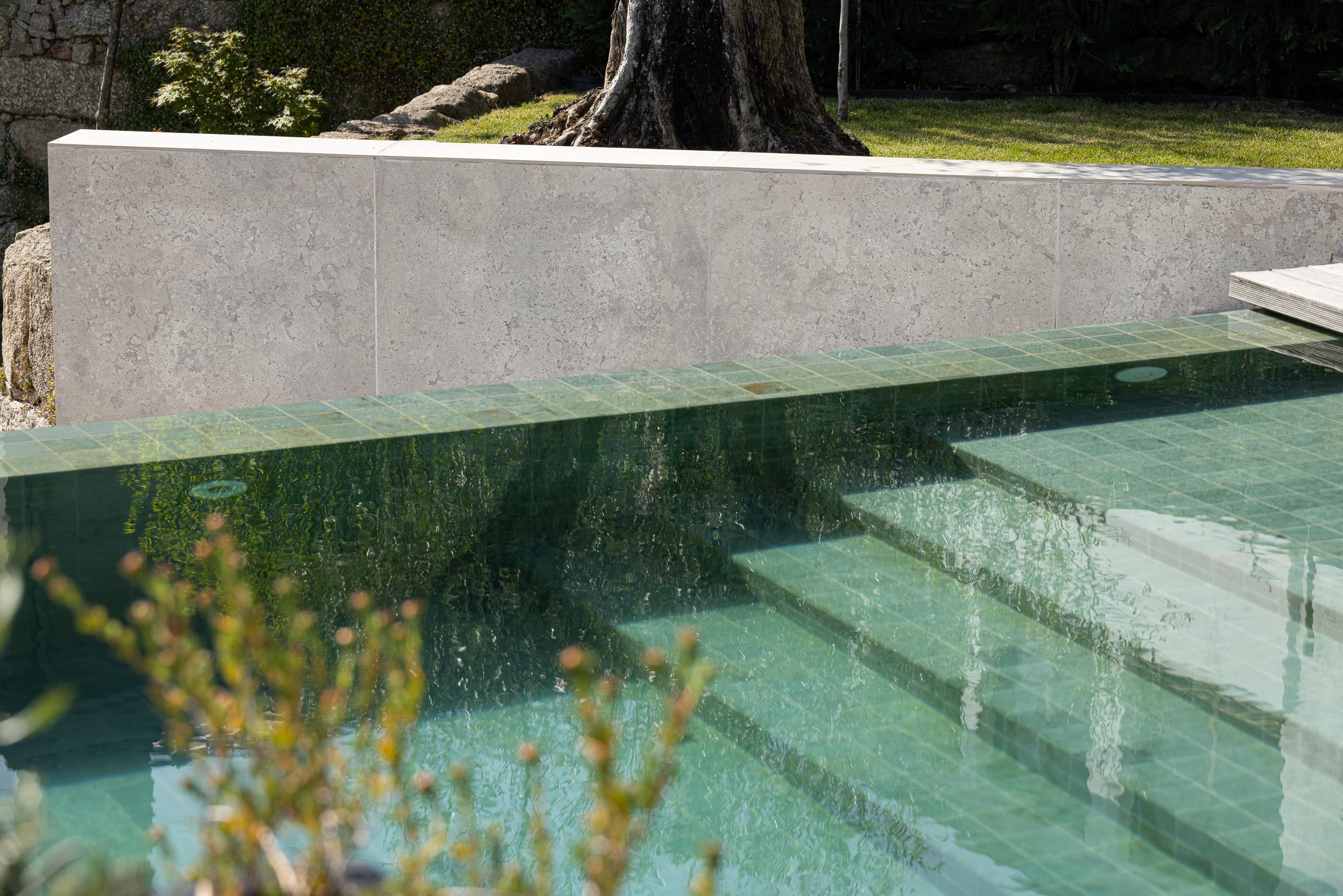 Piscina: Detalhe da piscina com mosaicos verdes e escadas, muro em pedra clara. — Moradia do Retiro arquitetura Ricardo Azevedo Arquitecto em Santo Tirso