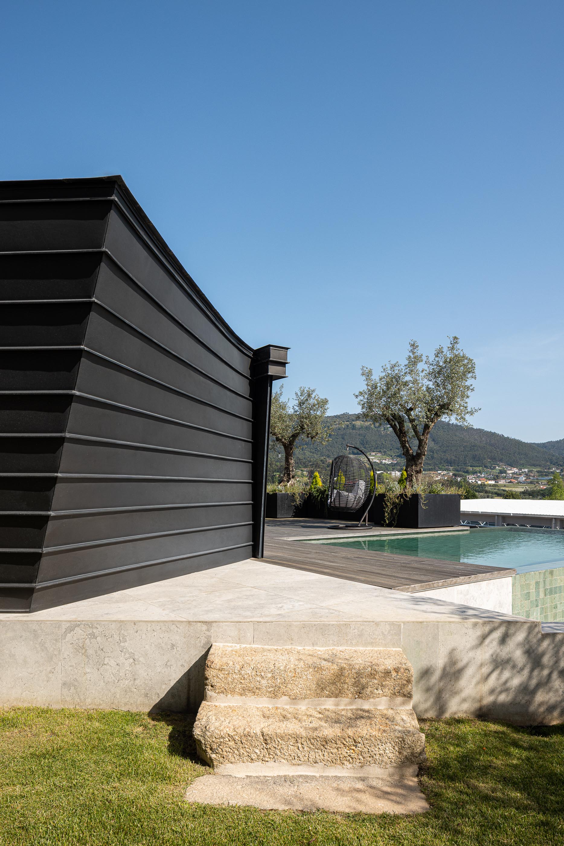 Exterior: Anexo moderno com revestimento metálico preto, terraço em madeira e piscina. — Moradia do Retiro arquitetura Ricardo Azevedo Arquitecto em Santo Tirso