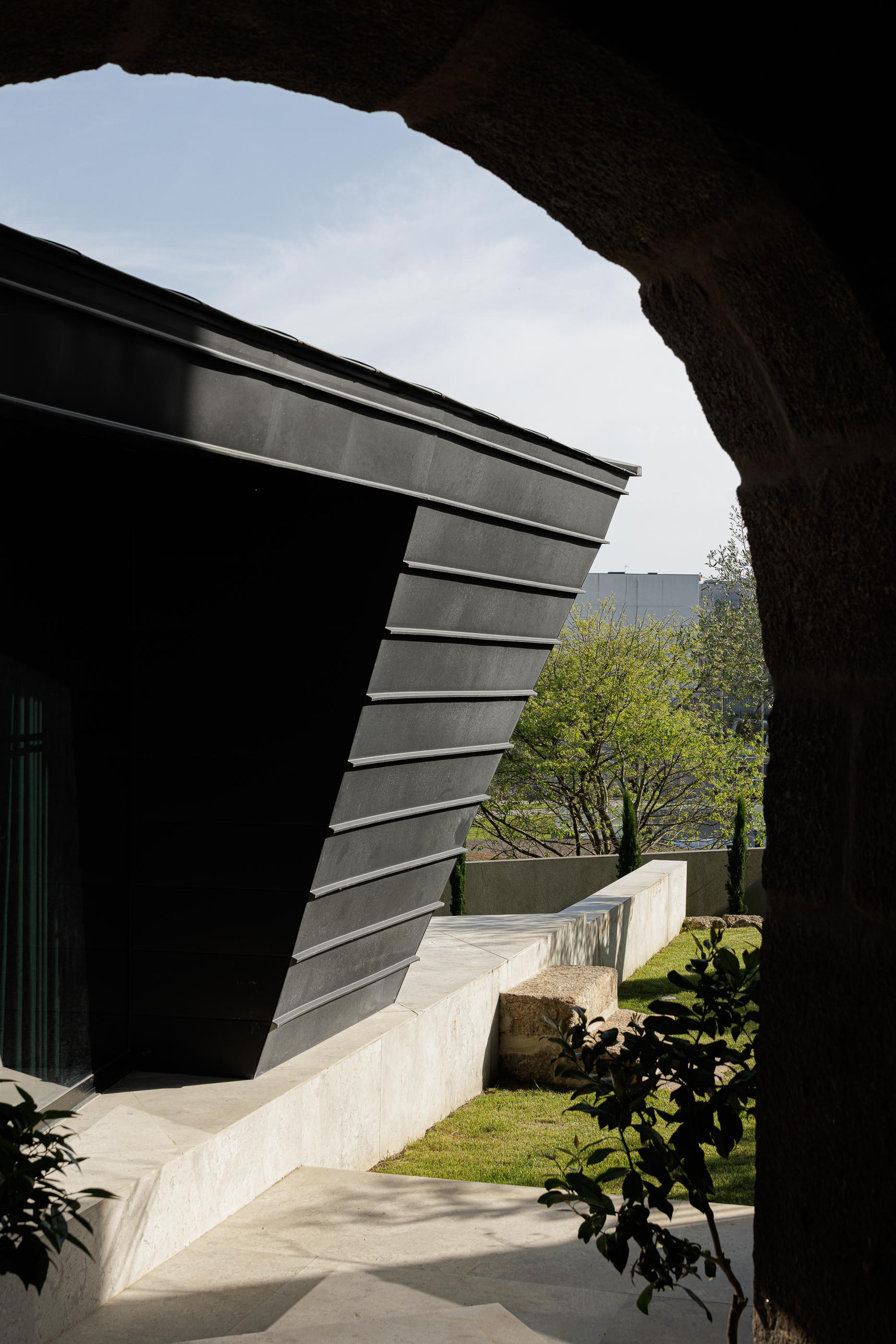 Exterior: Anexo moderno com revestimento metálico preto, visto através de arco de pedra. — Moradia do Retiro arquitetura Ricardo Azevedo Arquitecto em Santo Tirso