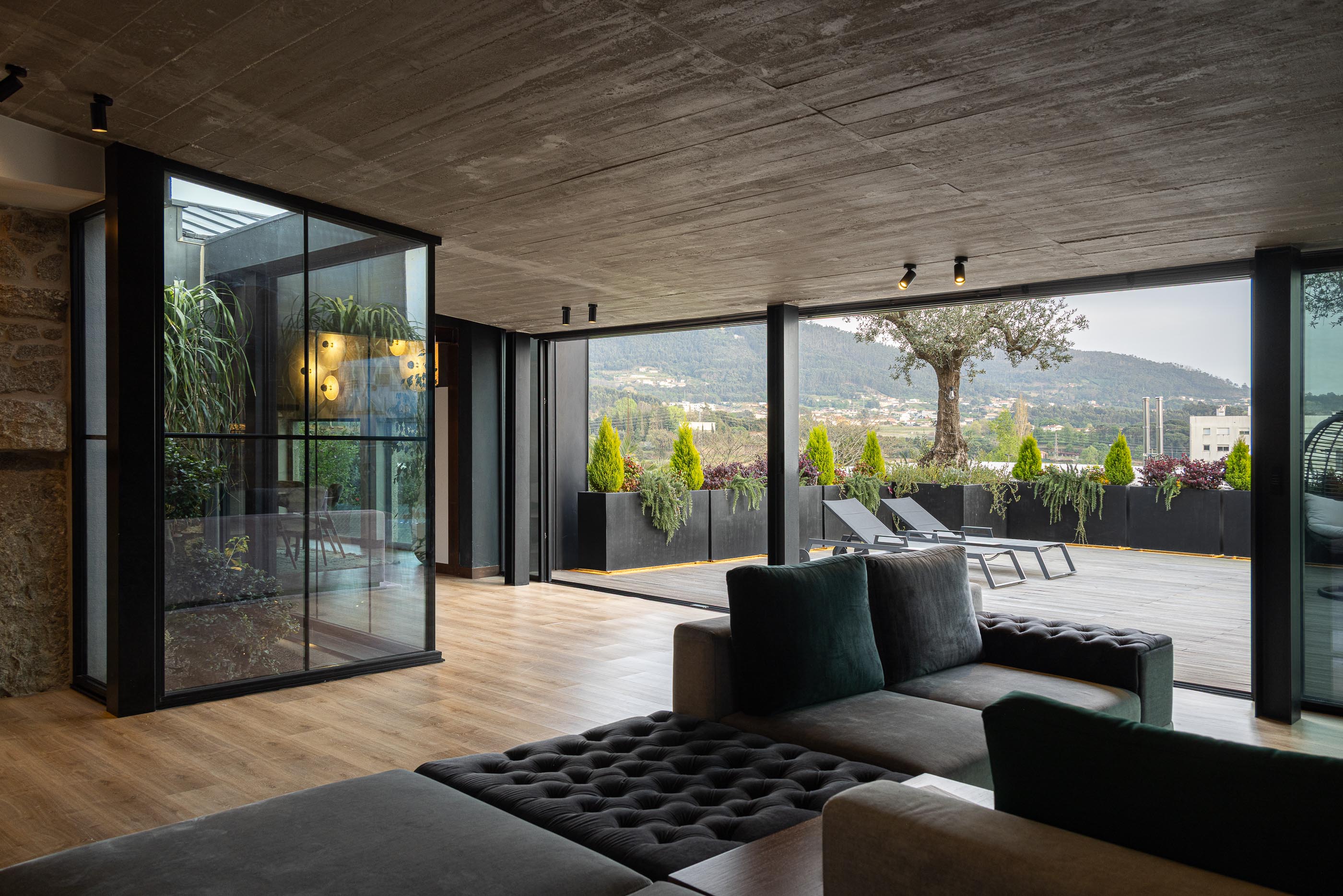 Sala de estar: Sofá modular cinza, teto em betão aparente, grandes janelas e vista para o terraço. — Moradia do Retiro arquitetura Ricardo Azevedo Arquitecto em Santo Tirso