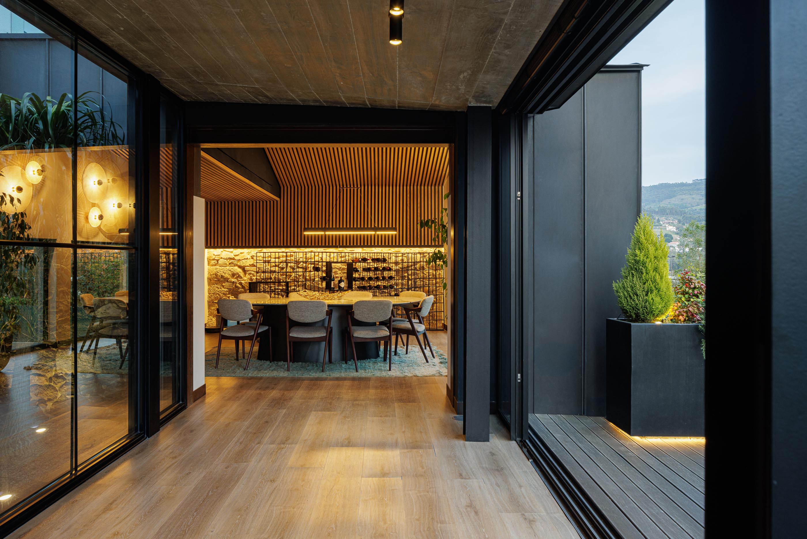 Sala de jantar: Vista da sala de jantar através de grandes janelas, teto em madeira e iluminação. — Moradia do Retiro arquitetura Ricardo Azevedo Arquitecto em Santo Tirso
