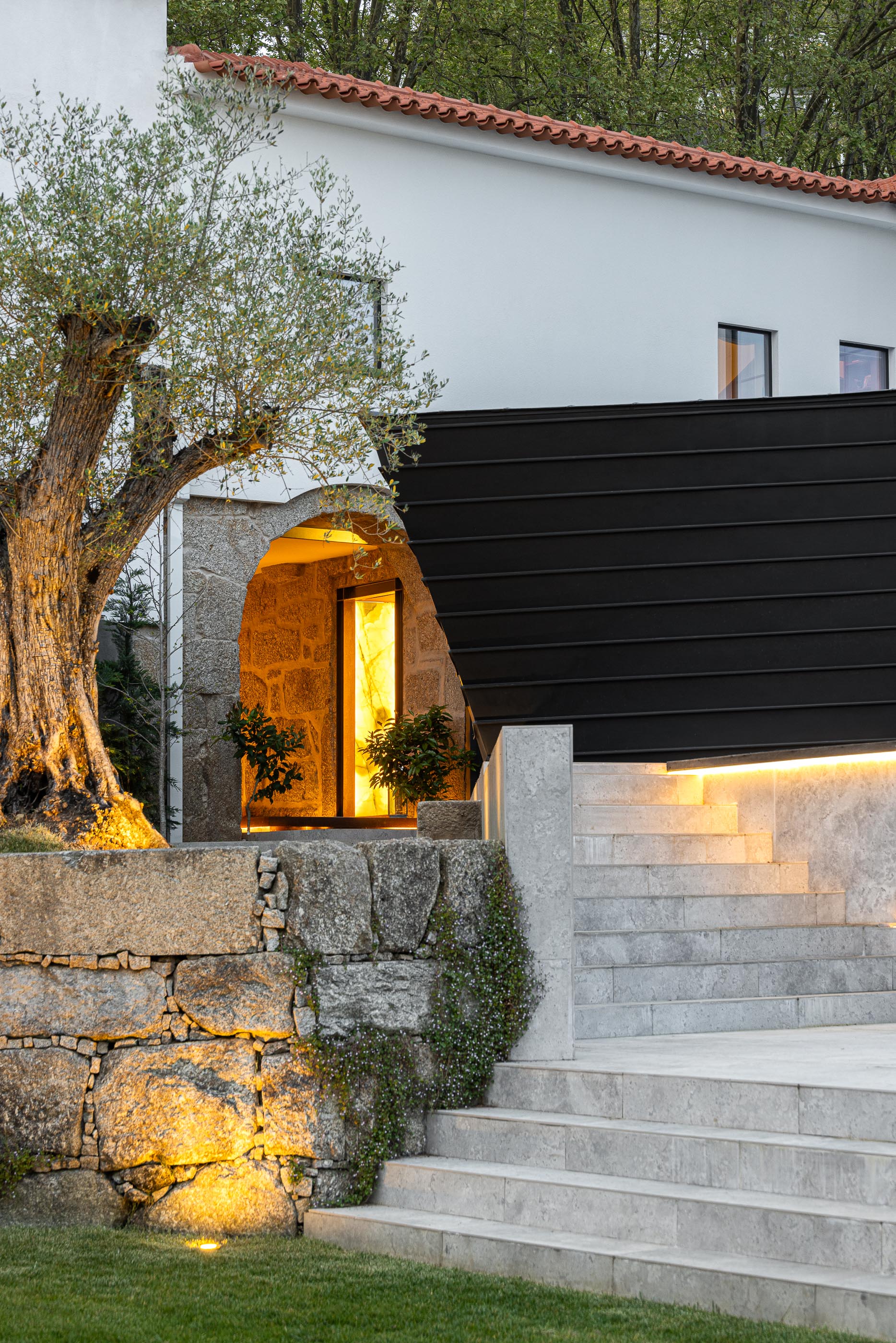 Exterior: Vista da entrada principal com iluminação e anexo moderno. — Moradia do Retiro arquitetura Ricardo Azevedo Arquitecto em Santo Tirso