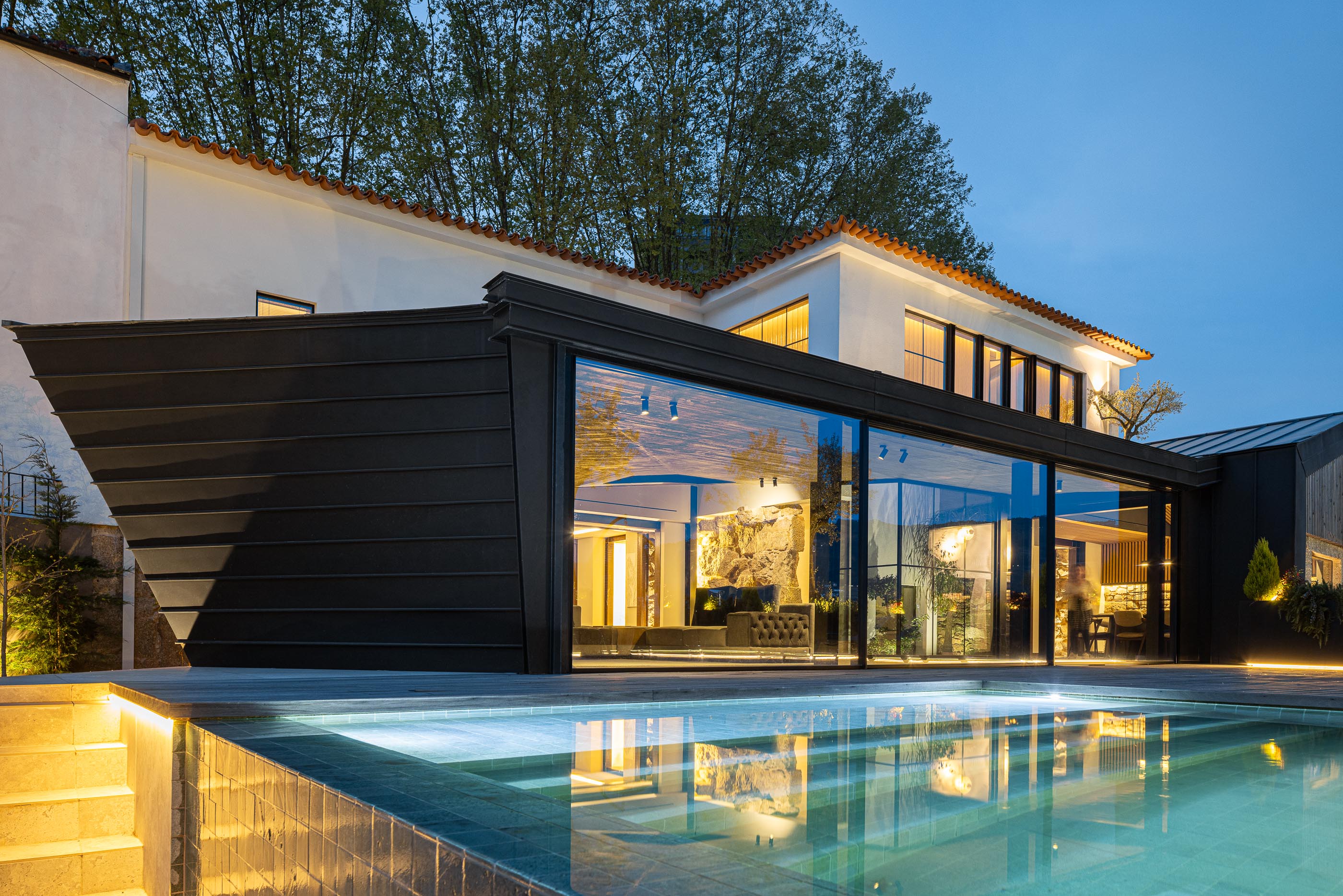 Exterior: Vista noturna da moradia com piscina refletindo a iluminação interior. — Moradia do Retiro arquitetura Ricardo Azevedo Arquitecto em Santo Tirso