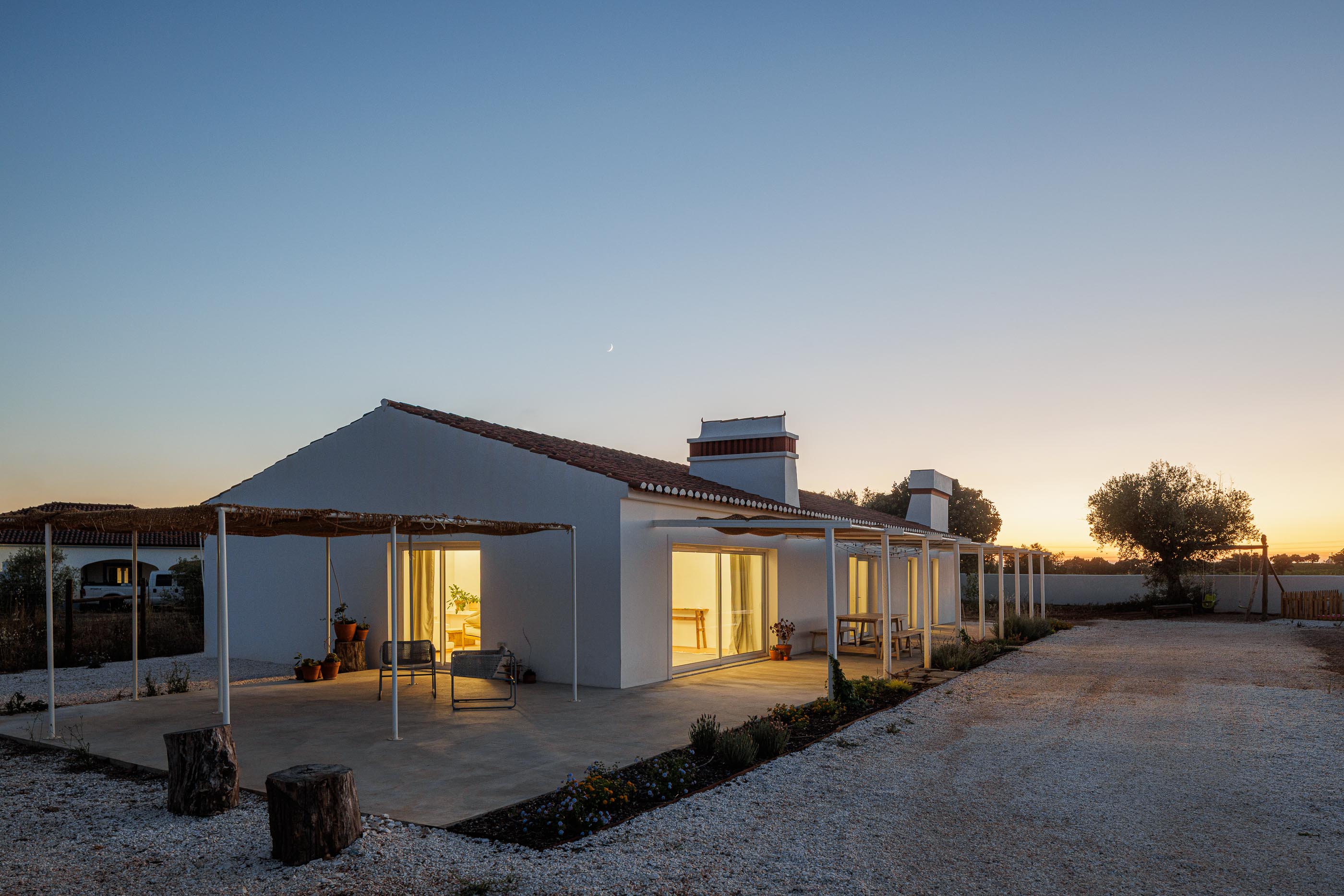 Exterior: Fachada branca com telhado de telha, alpendre com cobertura de palha e gravilha no pavimento. — Monte do Divor arquitetura Vasco Burnay Arquitectura em Estremoz