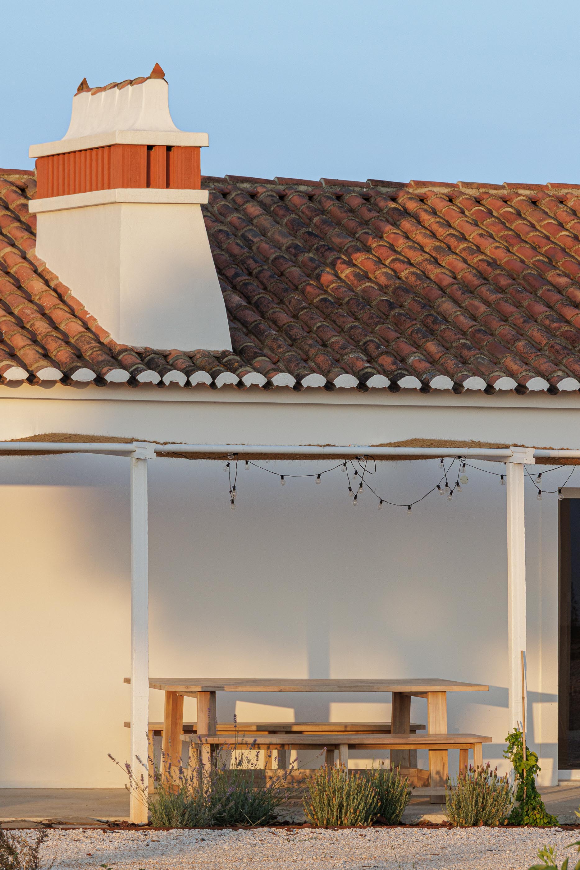 Exterior: Detalhe da chaminé em tijolo vermelho e telhado de telha, com alpendre e mesa de madeira. — Monte do Divor arquitetura Vasco Burnay Arquitectura em Estremoz