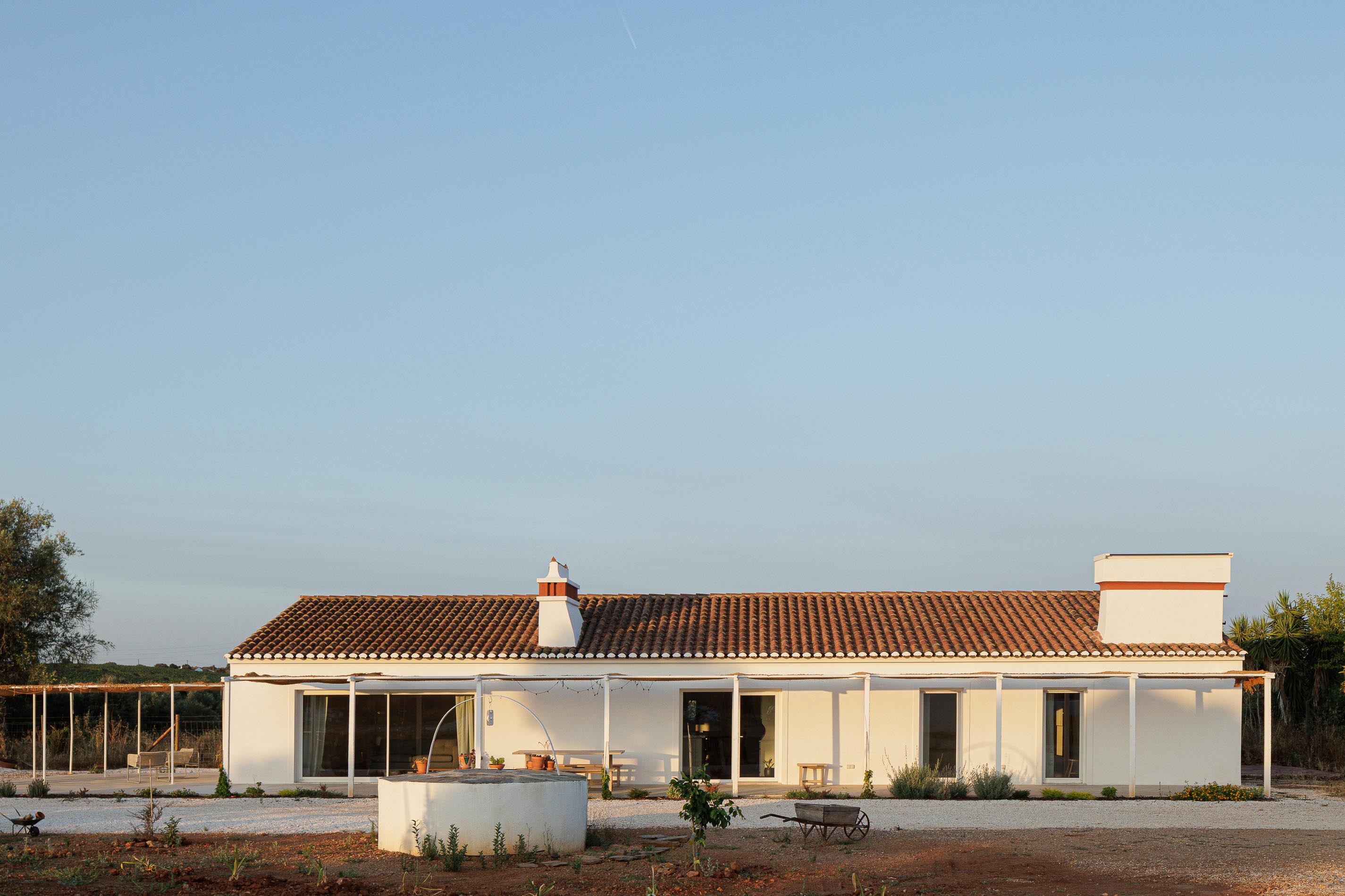 Exterior: Vista geral da casa branca com telhado de telha, alpendre e terreno com gravilha. — Monte do Divor arquitetura Vasco Burnay Arquitectura em Estremoz