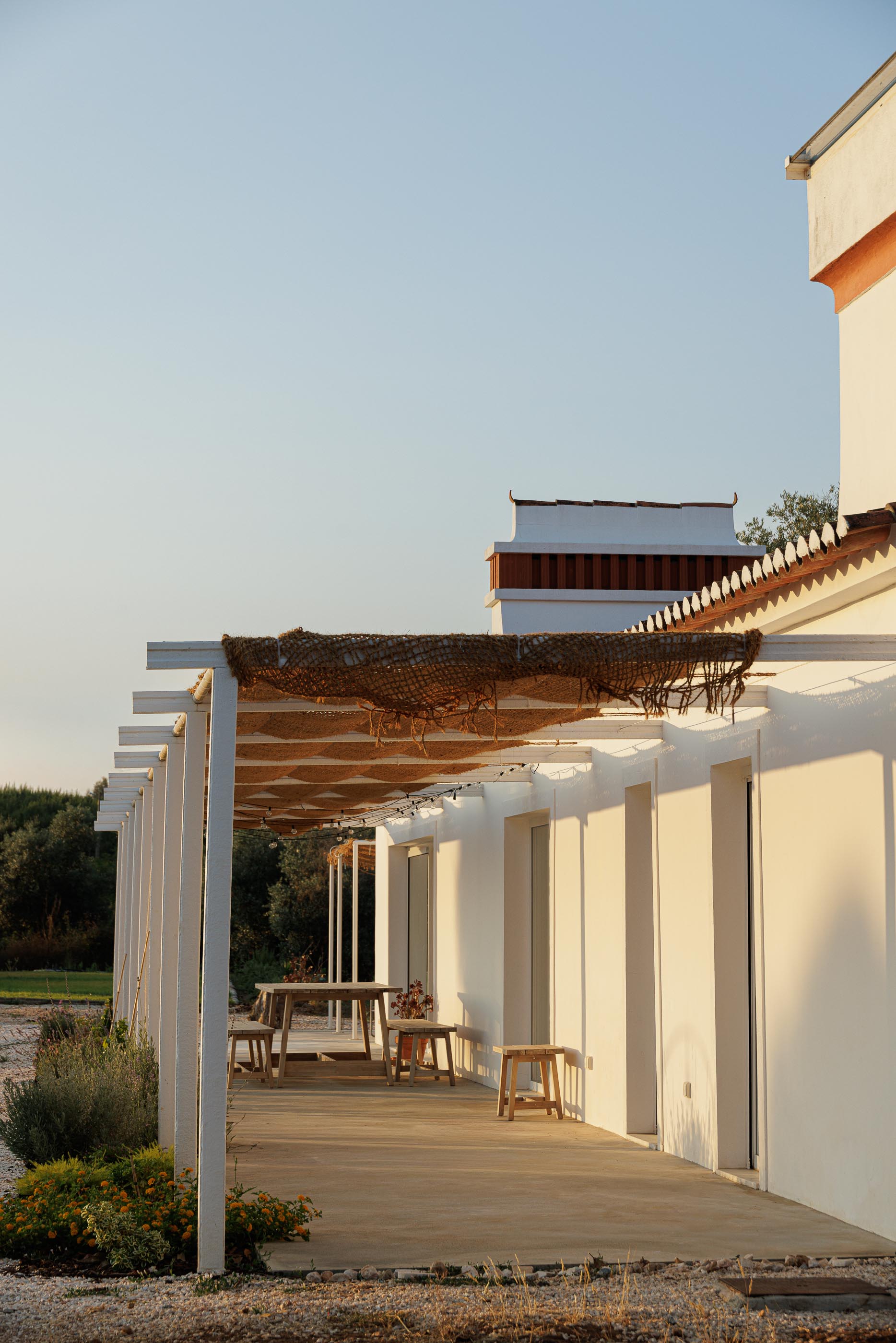 Exterior: Alpendre com pavimento em madeira, mesa e cadeiras de madeira, e fachada branca. — Monte do Divor arquitetura Vasco Burnay Arquitectura em Estremoz