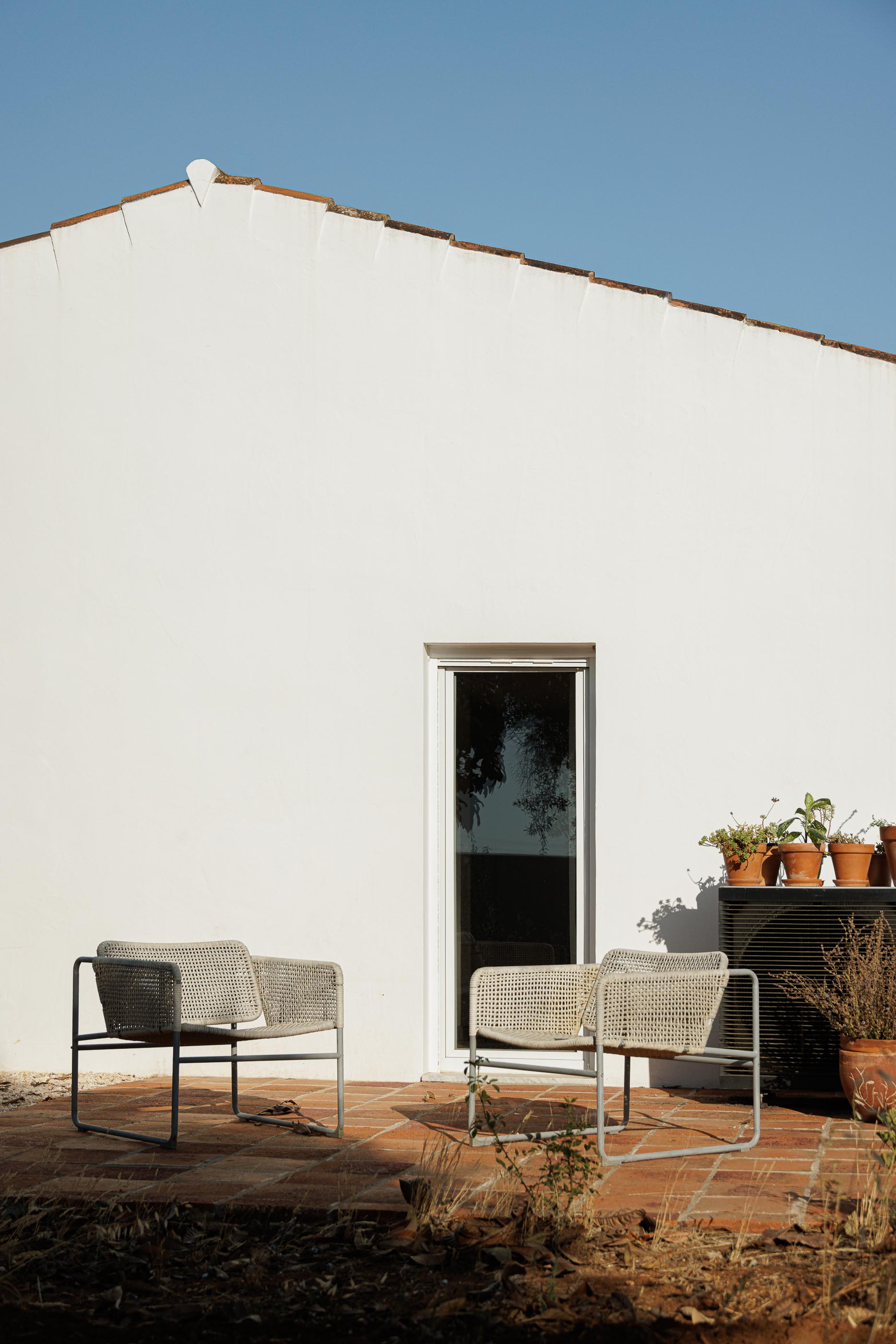 Exterior: Fachada branca com cadeiras de corda, vasos de plantas e pavimento em tijoleira. — Monte do Divor arquitetura Vasco Burnay Arquitectura em Estremoz