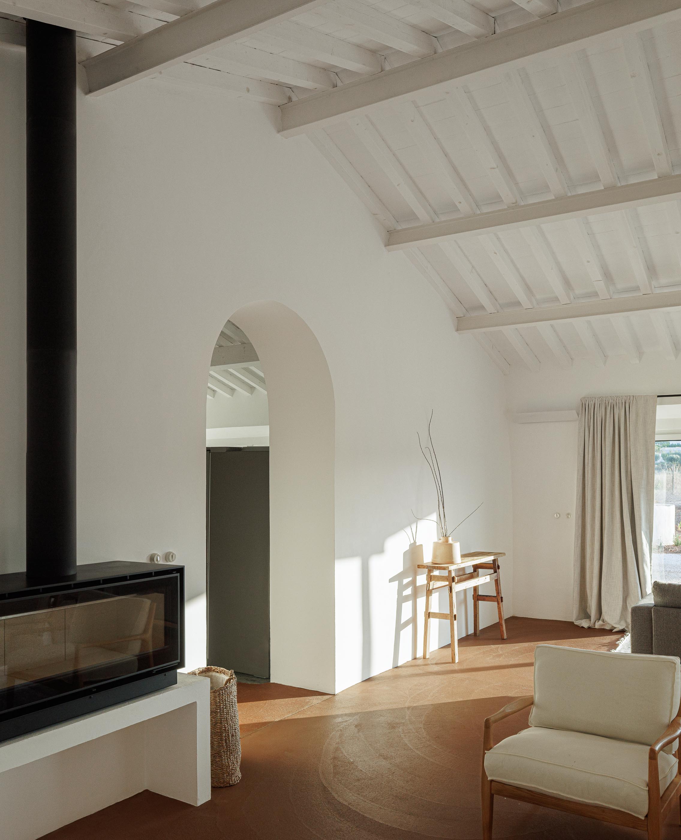 Sala de estar: Lareira moderna, pavimento em tijoleira, teto branco com vigas e mobiliário minimalista. — Monte do Divor arquitetura Vasco Burnay Arquitectura em Estremoz