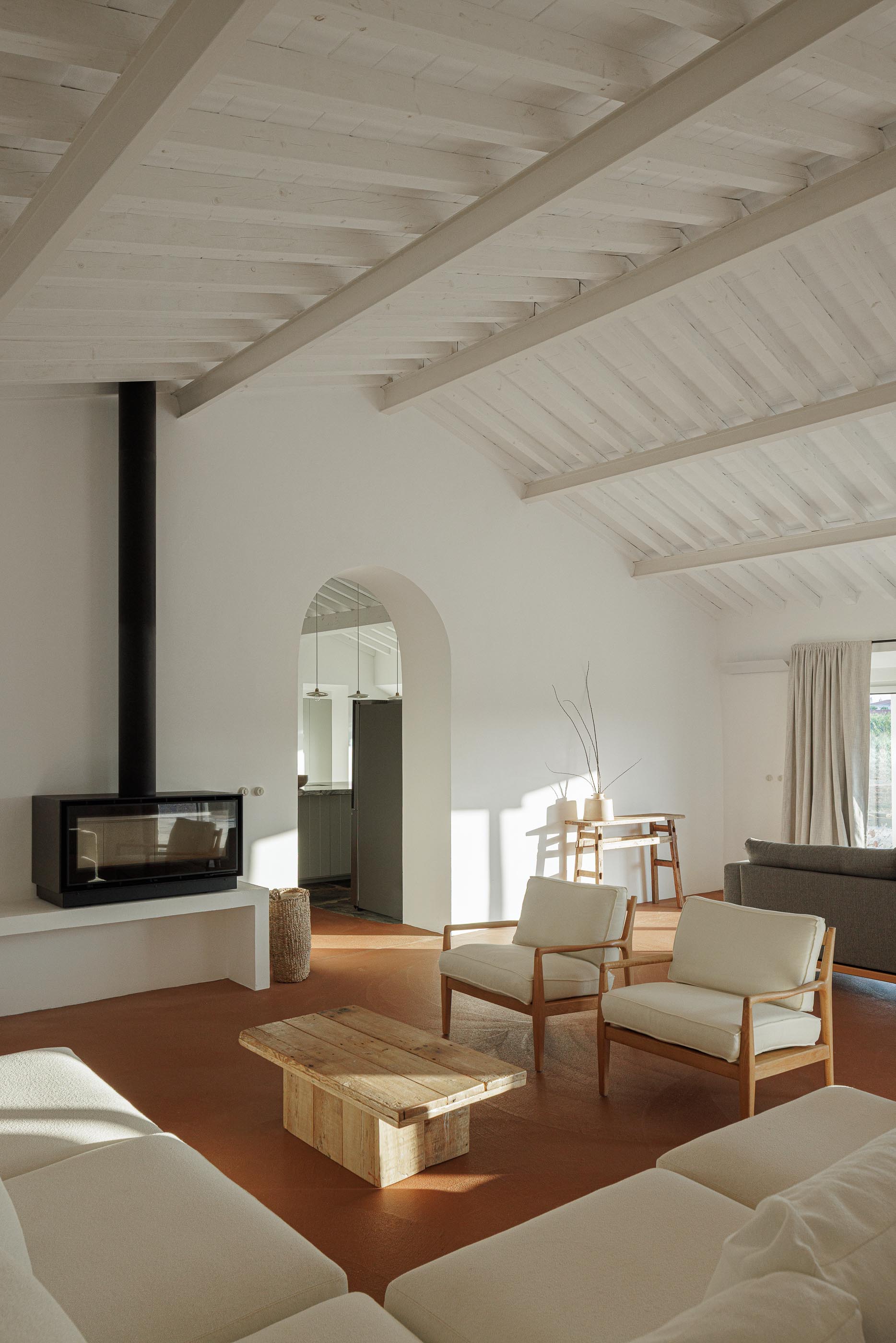 Sala de estar: Sofá branco, cadeiras de madeira, lareira e teto branco com vigas de madeira. — Monte do Divor arquitetura Vasco Burnay Arquitectura em Estremoz