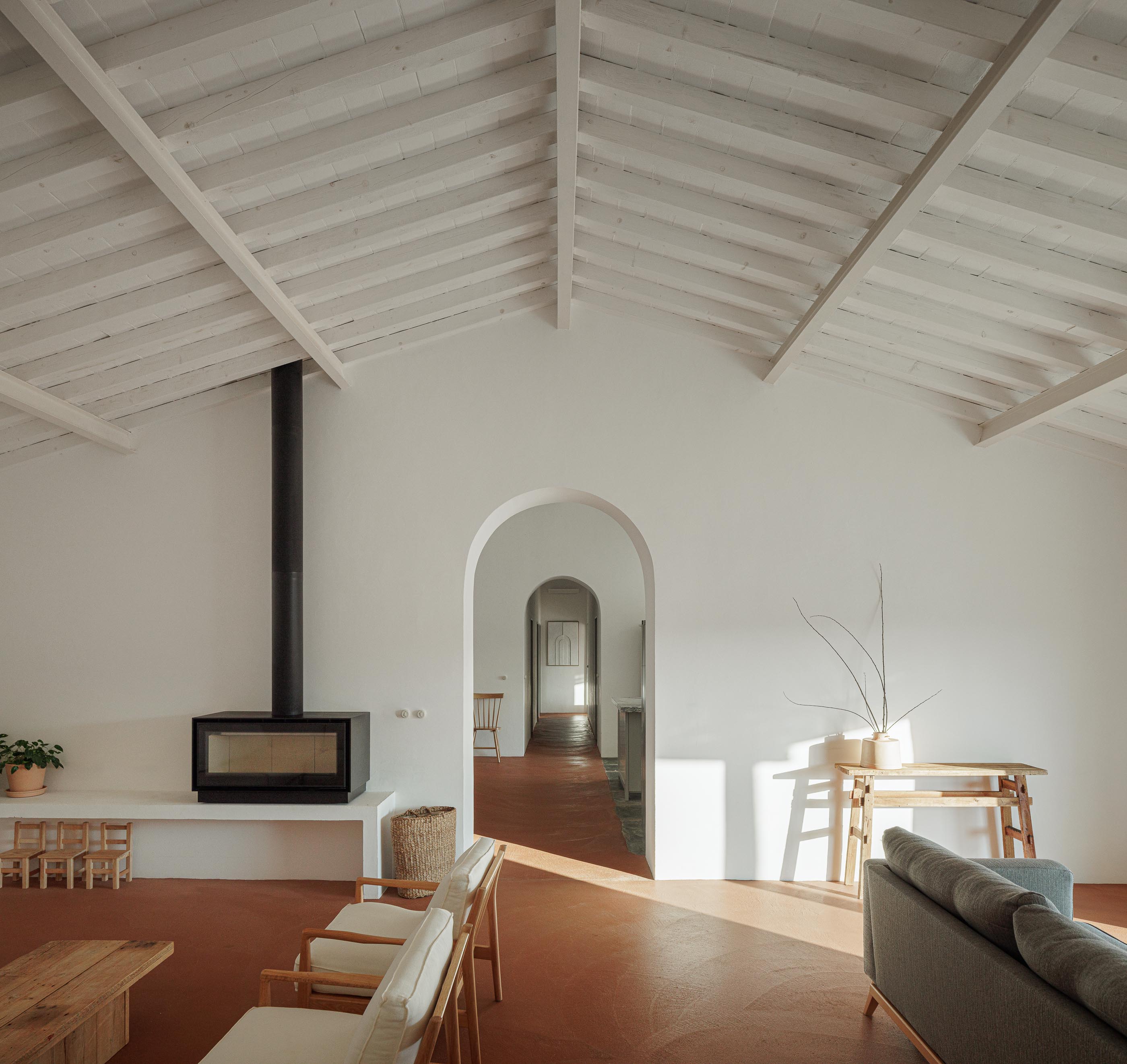 Sala de estar: Vista ampla com lareira, sofás, cadeiras de madeira e teto branco com vigas de madeira. — Monte do Divor arquitetura Vasco Burnay Arquitectura em Estremoz