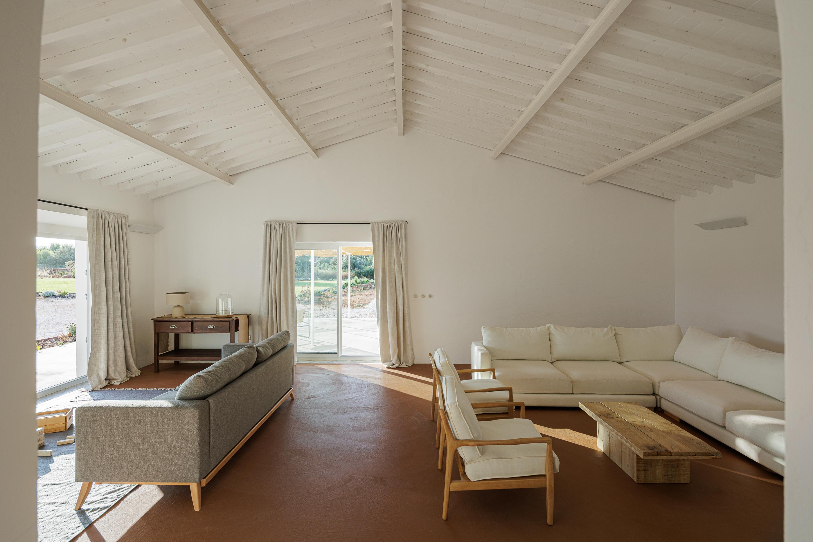 Sala de estar: Sofás, cadeiras de madeira, pavimento em tijoleira e teto branco com vigas de madeira. — Monte do Divor arquitetura Vasco Burnay Arquitectura em Estremoz