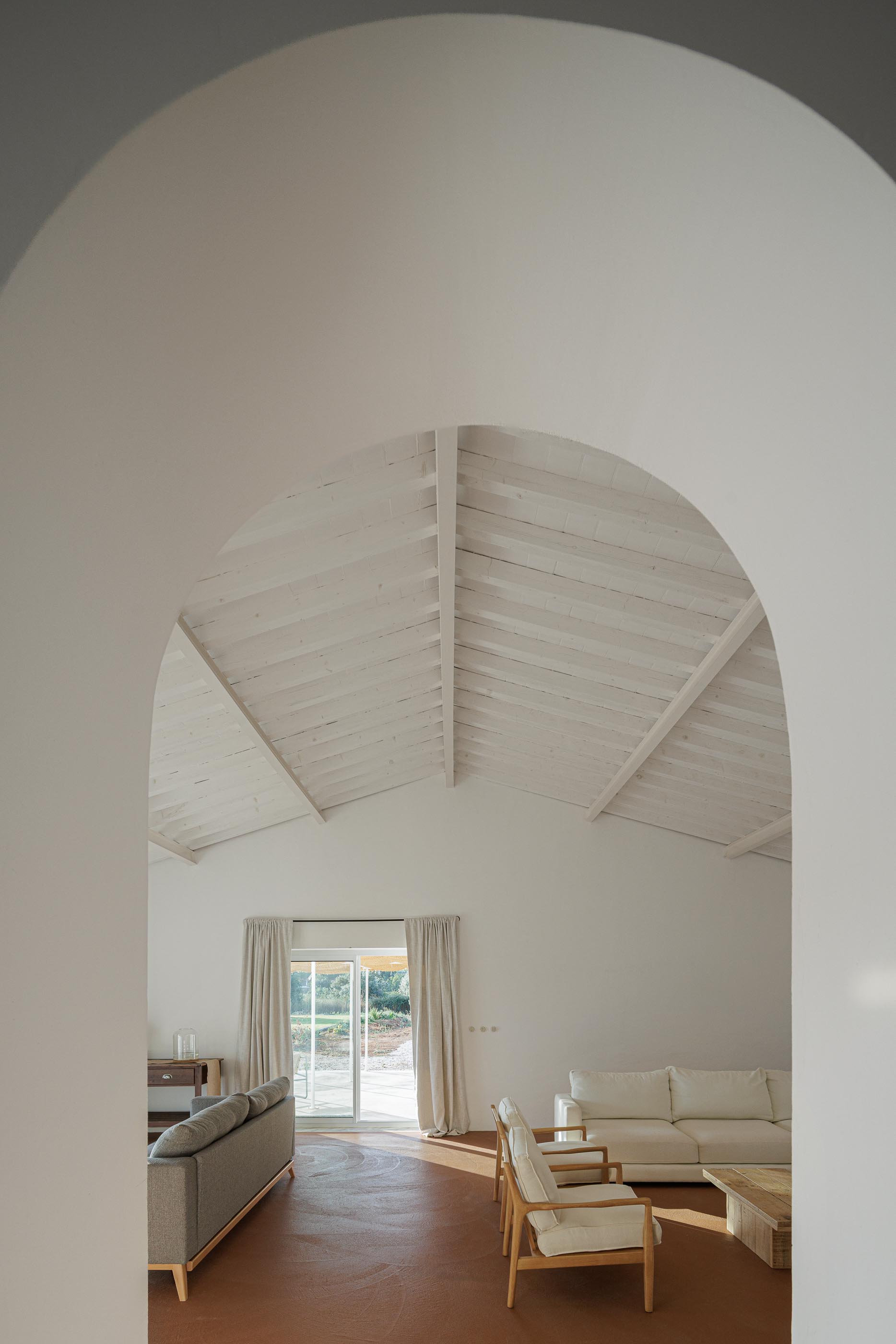 Sala de estar: Vista através de um arco para a sala, com pavimento em tijoleira e teto branco com vigas. — Monte do Divor arquitetura Vasco Burnay Arquitectura em Estremoz