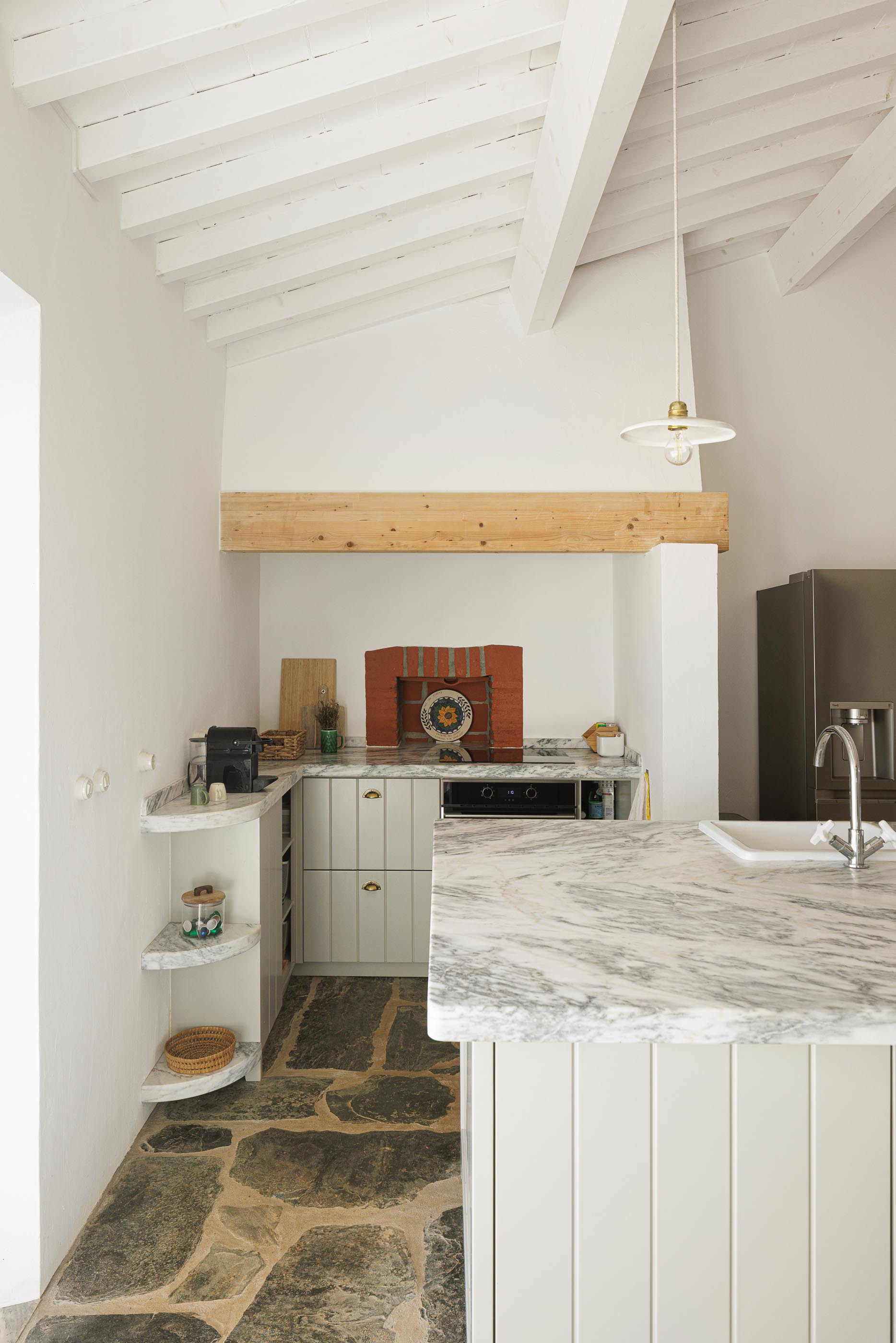 Cozinha: Bancada em mármore, pavimento em pedra rústica e teto branco com vigas de madeira. — Monte do Divor arquitetura Vasco Burnay Arquitectura em Estremoz