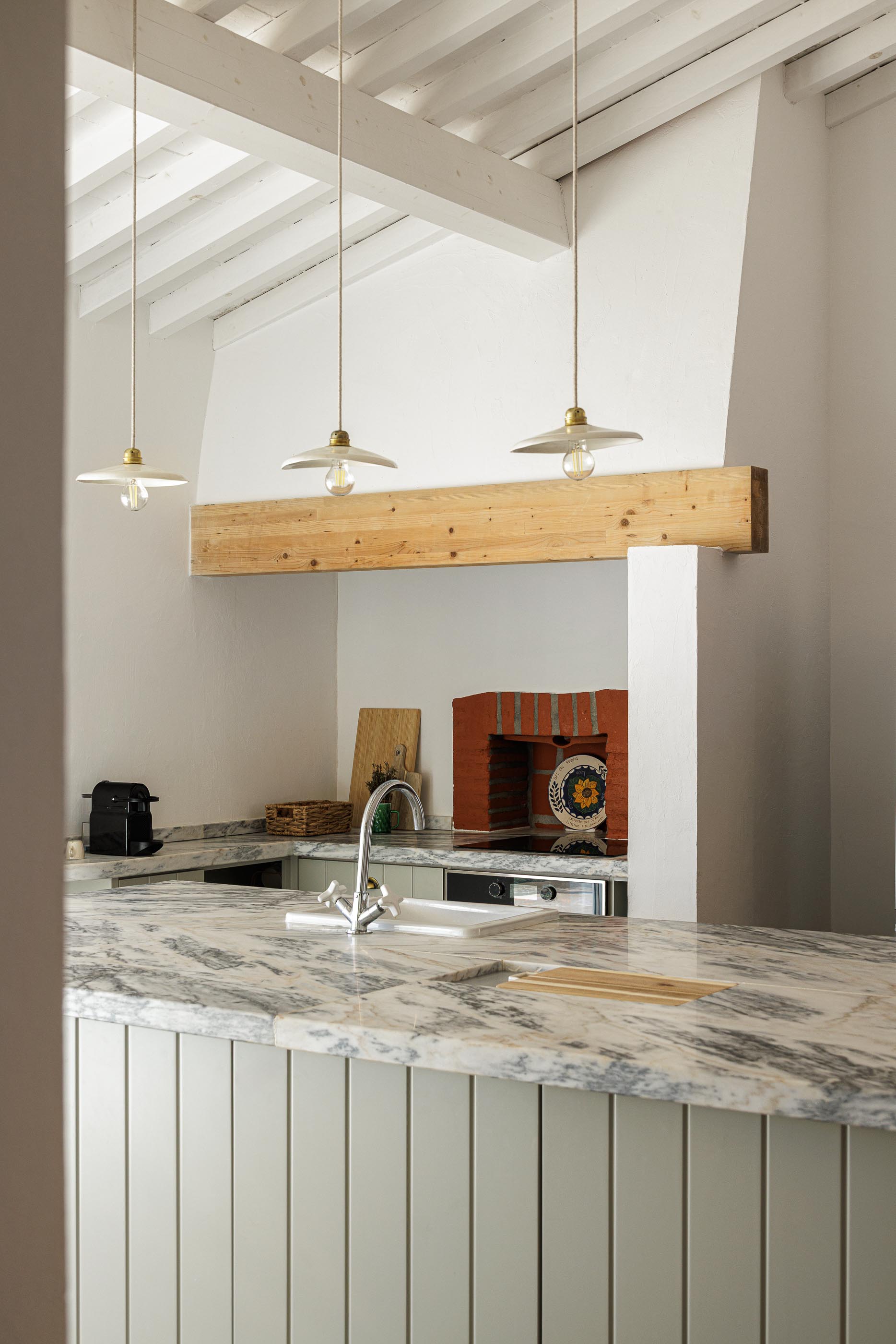 Cozinha: Bancada em mármore, candeeiros suspensos e teto branco com vigas de madeira. — Monte do Divor arquitetura Vasco Burnay Arquitectura em Estremoz