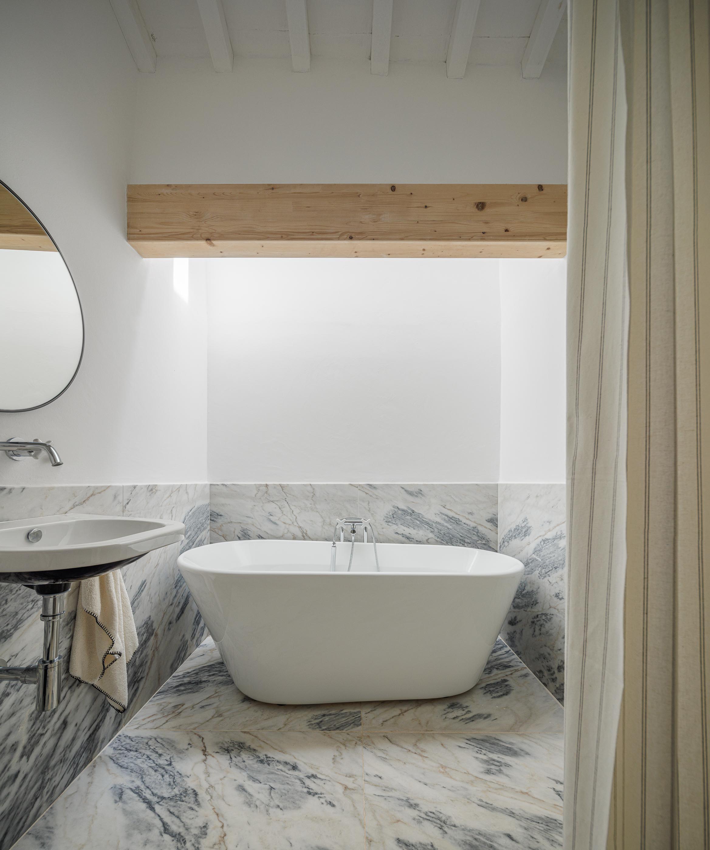 Casa de banho: Banheira branca, lavatório suspenso e revestimento em mármore. — Monte do Divor arquitetura Vasco Burnay Arquitectura em Estremoz