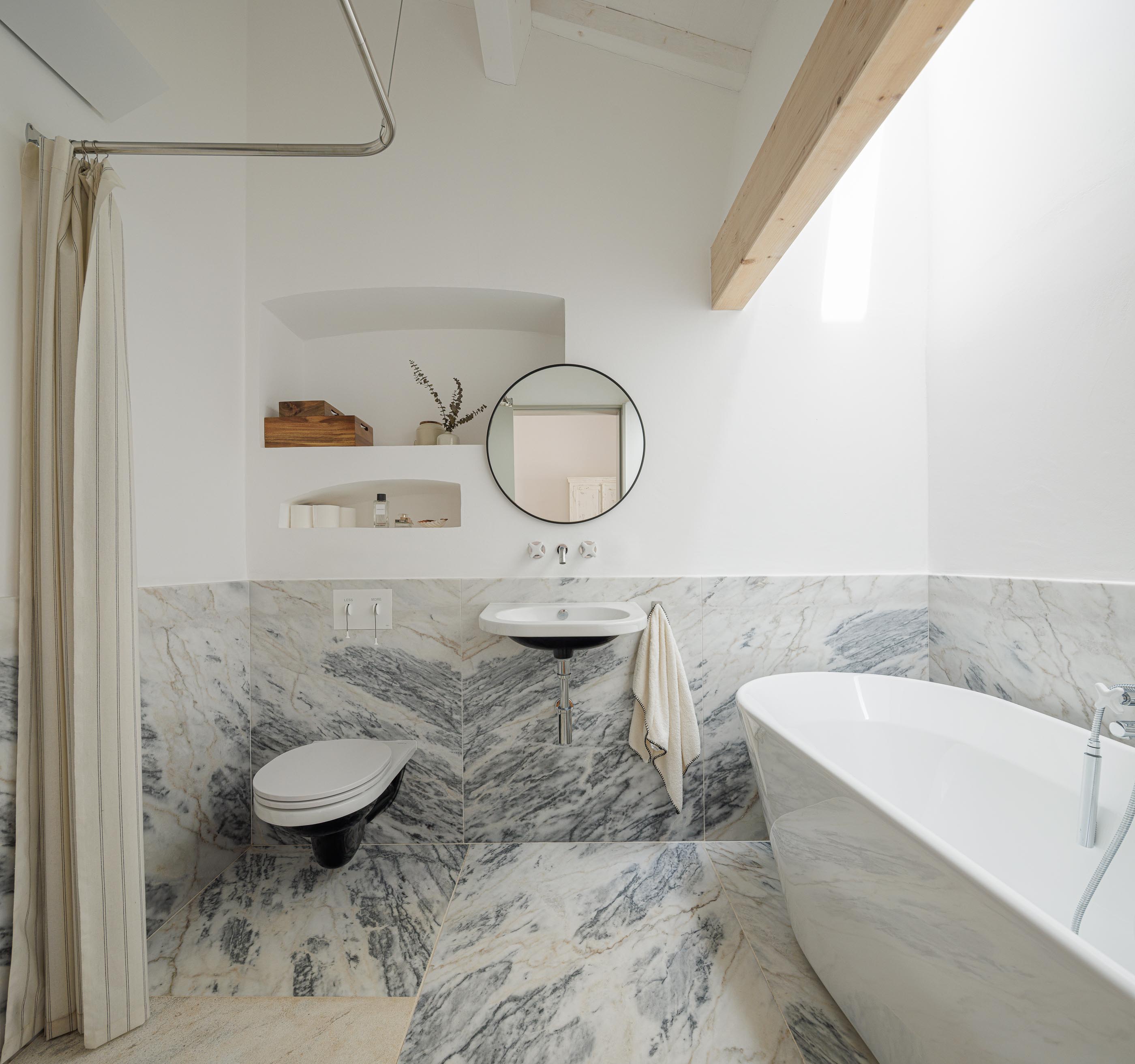 Casa de banho: Banheira branca, lavatório suspenso, sanita suspensa e revestimento em mármore. — Monte do Divor arquitetura Vasco Burnay Arquitectura em Estremoz